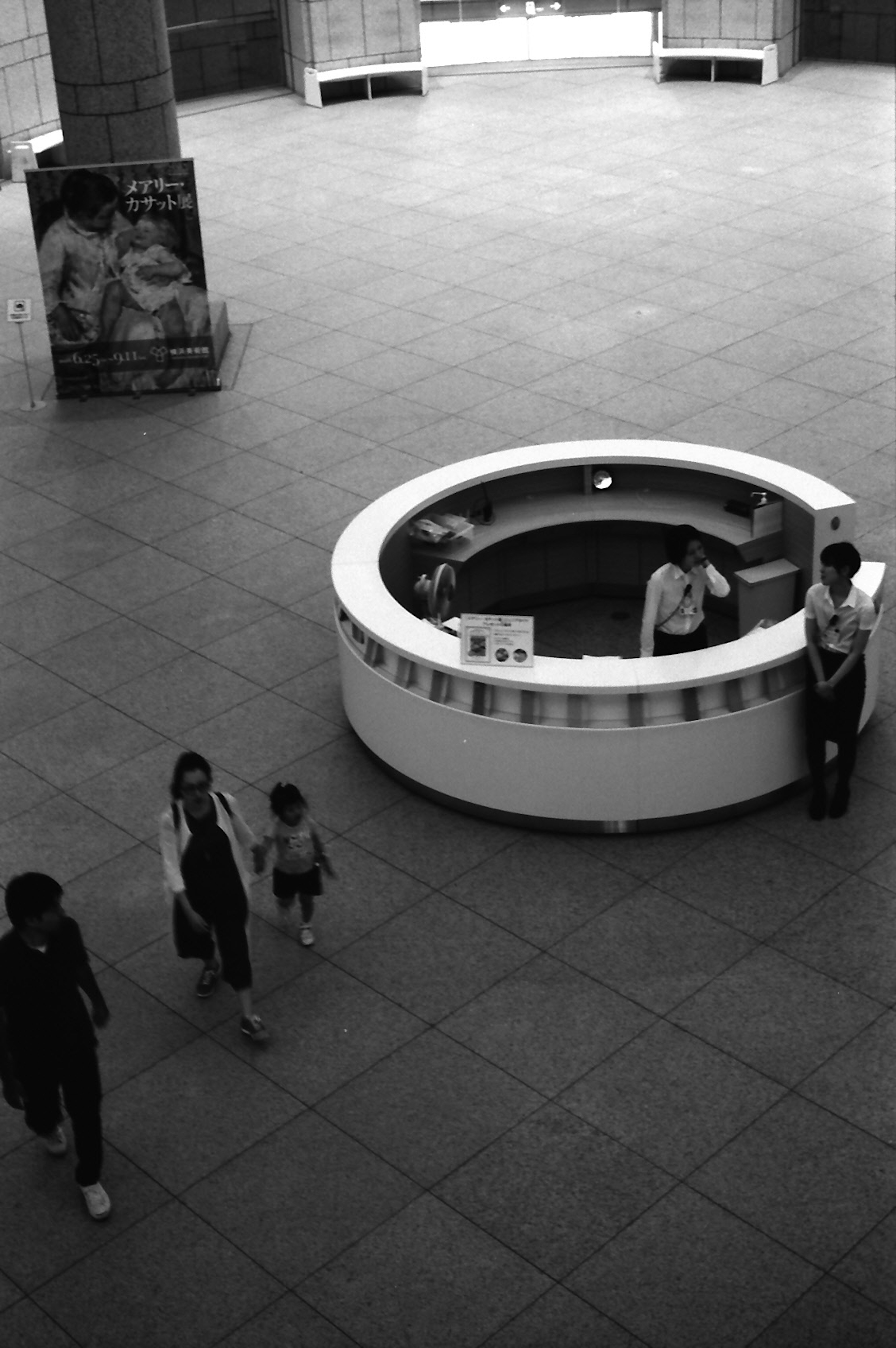 Imagen en blanco y negro de un mostrador de recepción circular con visitantes