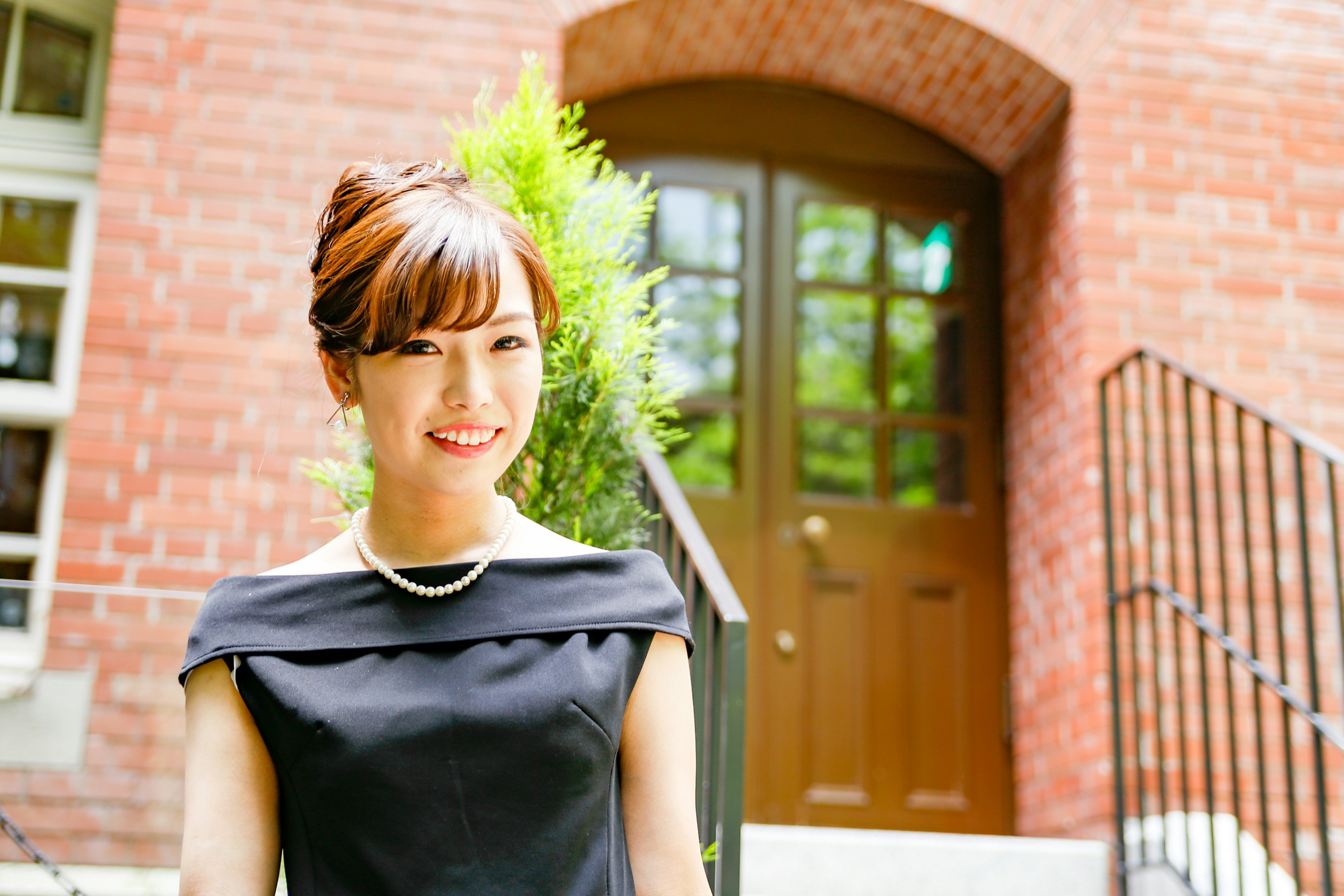 A woman in a black dress smiling in front of a brick building