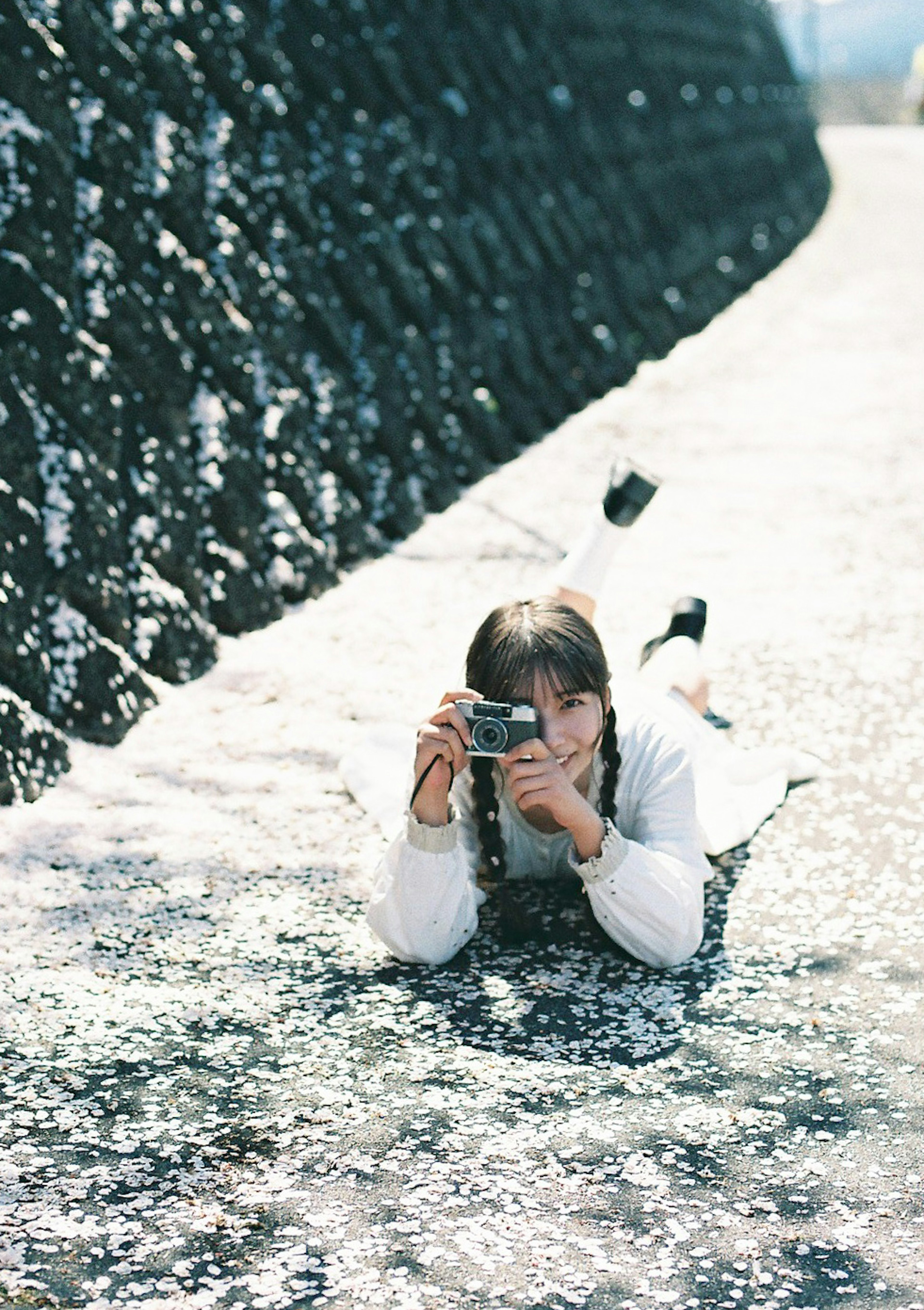 Girl lying by the water holding a camera wearing white clothes and black shoes reflections on the water surface