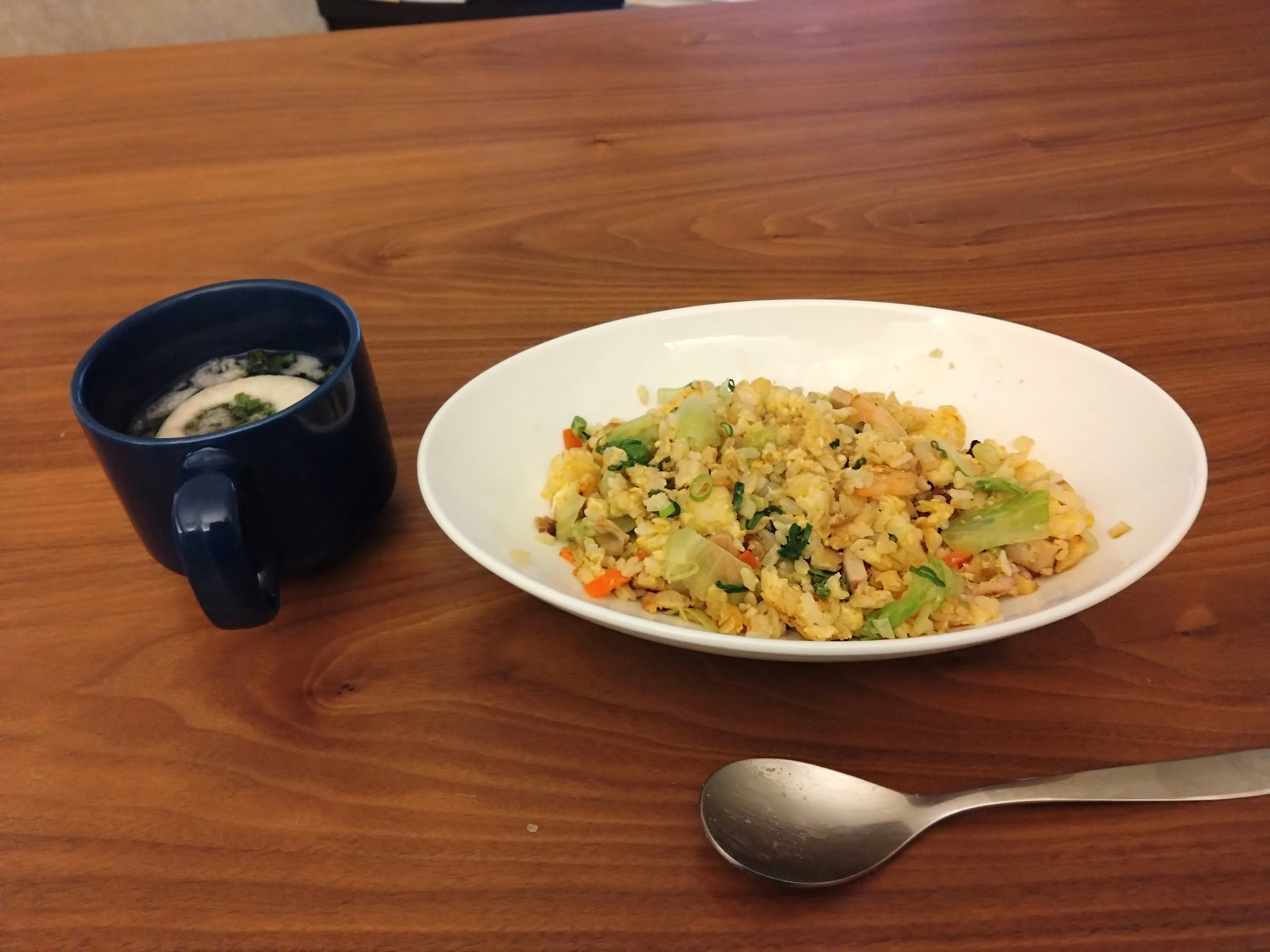 A blue cup of soup next to a plate of vegetable fried rice