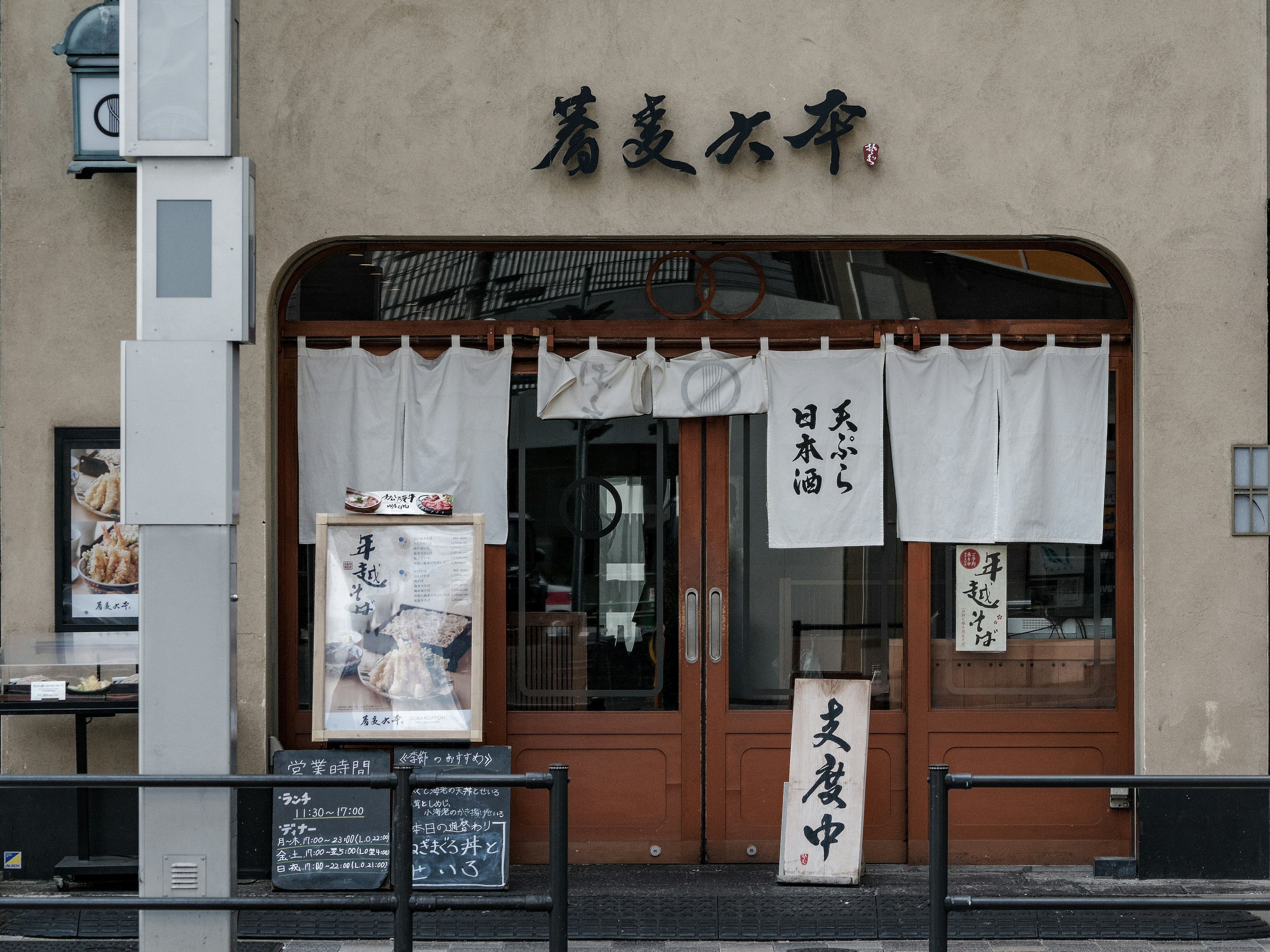 Fassade eines traditionellen japanischen Restaurants mit Holztüren und Noren-Vorhängen Menütafel