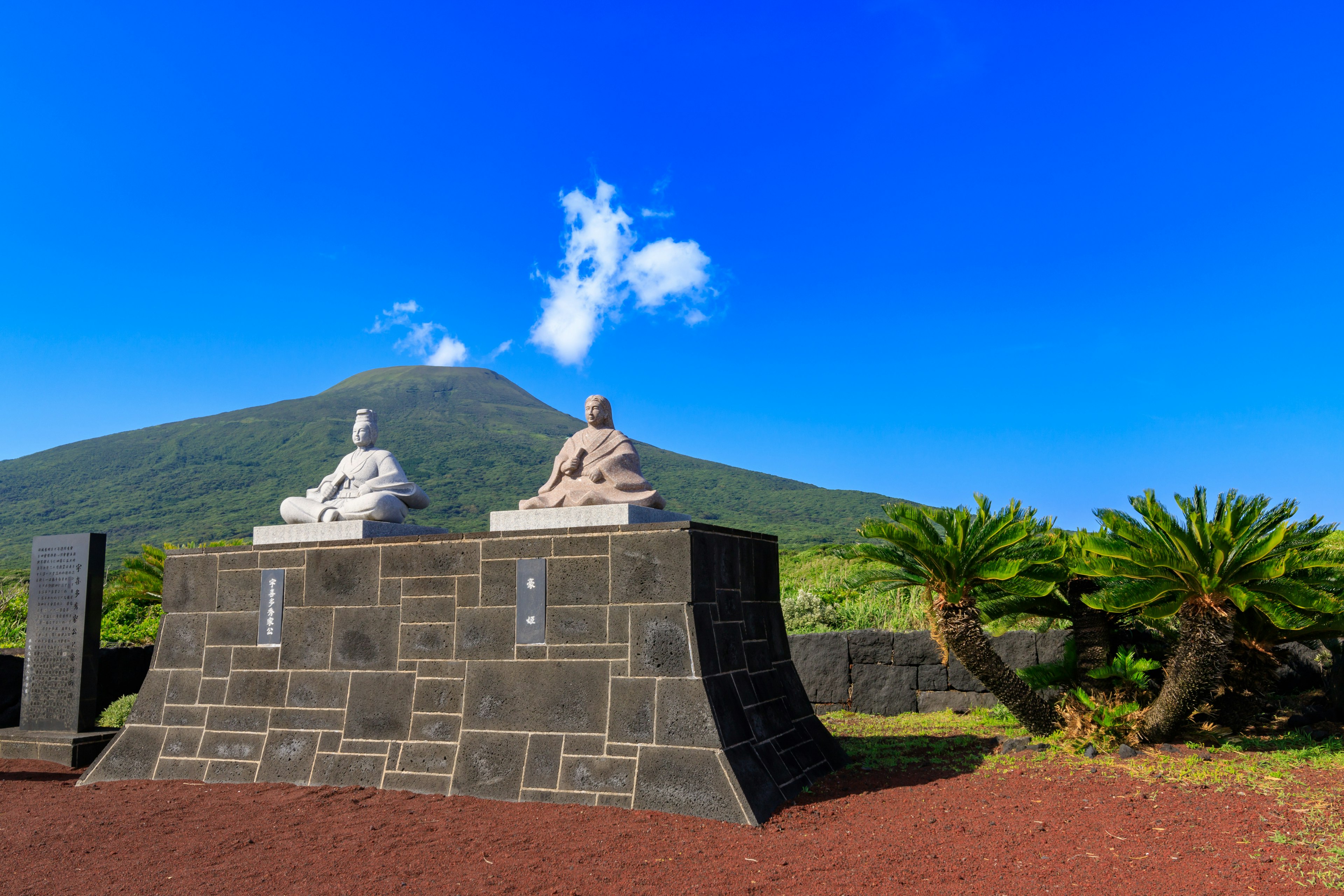 Zwei Statuen in einer Landschaft mit blauem Himmel und Berg