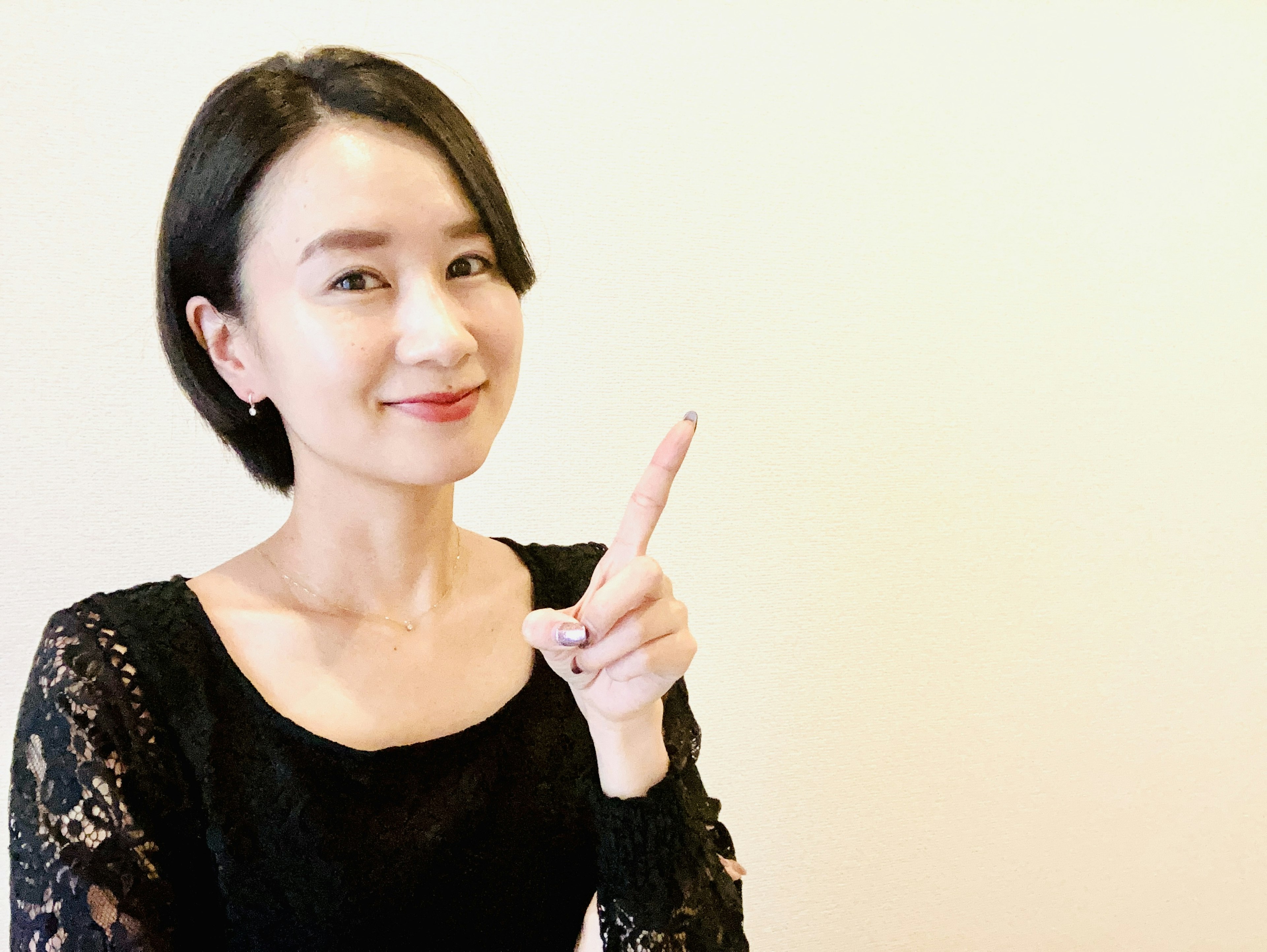 A woman in a black lace dress smiling and pointing with her finger