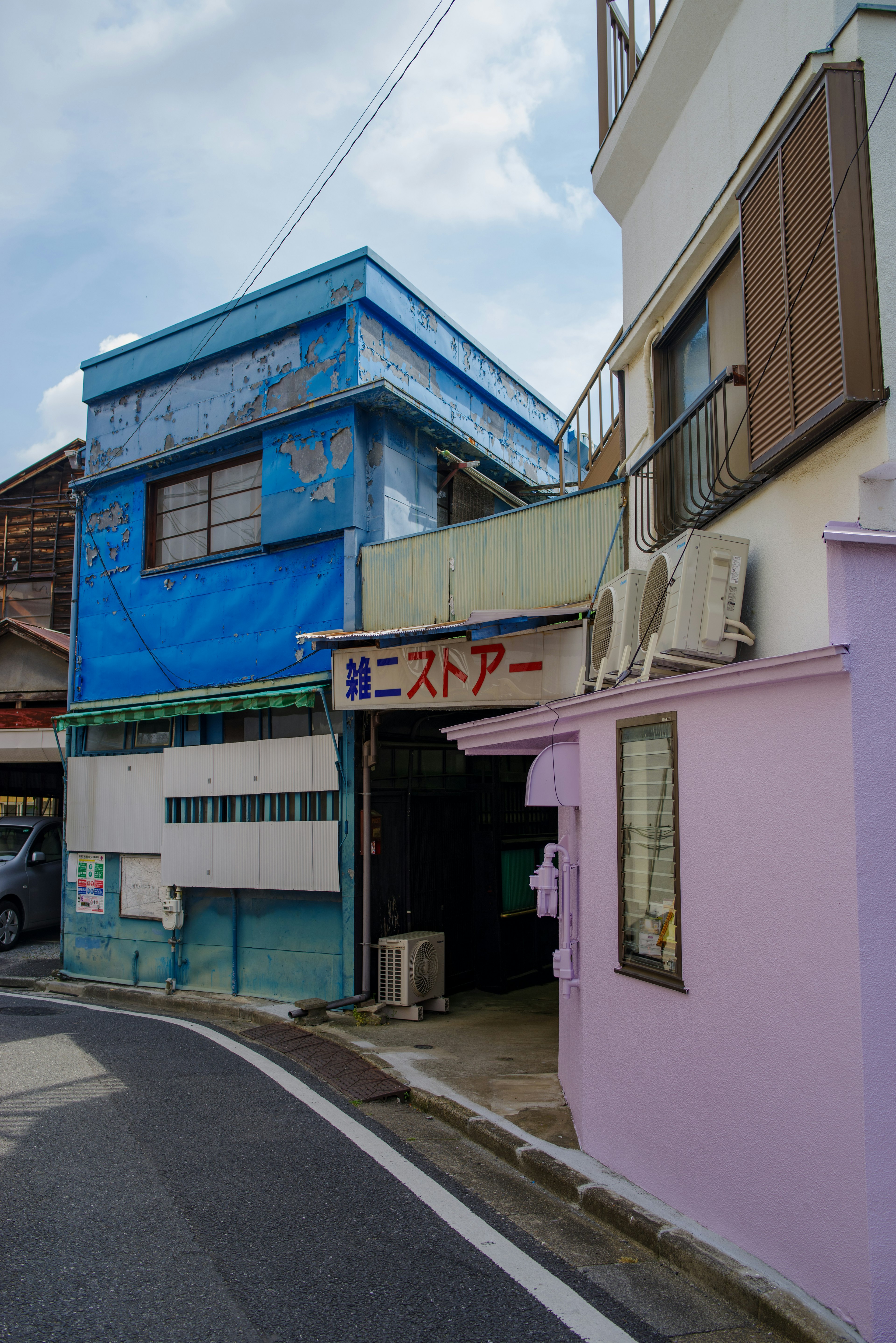 Escena de calle estrecha con un edificio azul y una tienda rosa