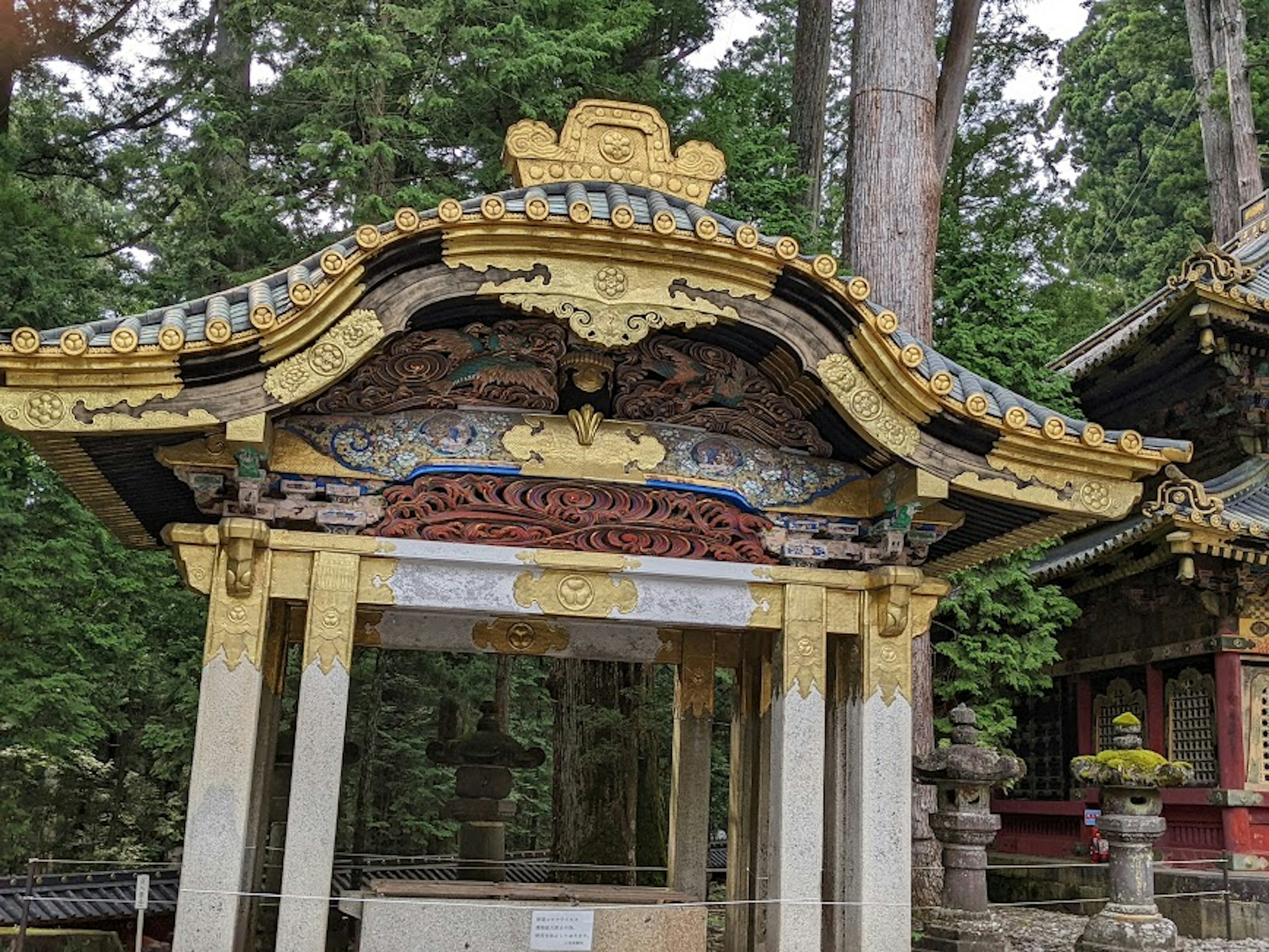 Intricately decorated shrine roof and pillars surrounded by lush greenery