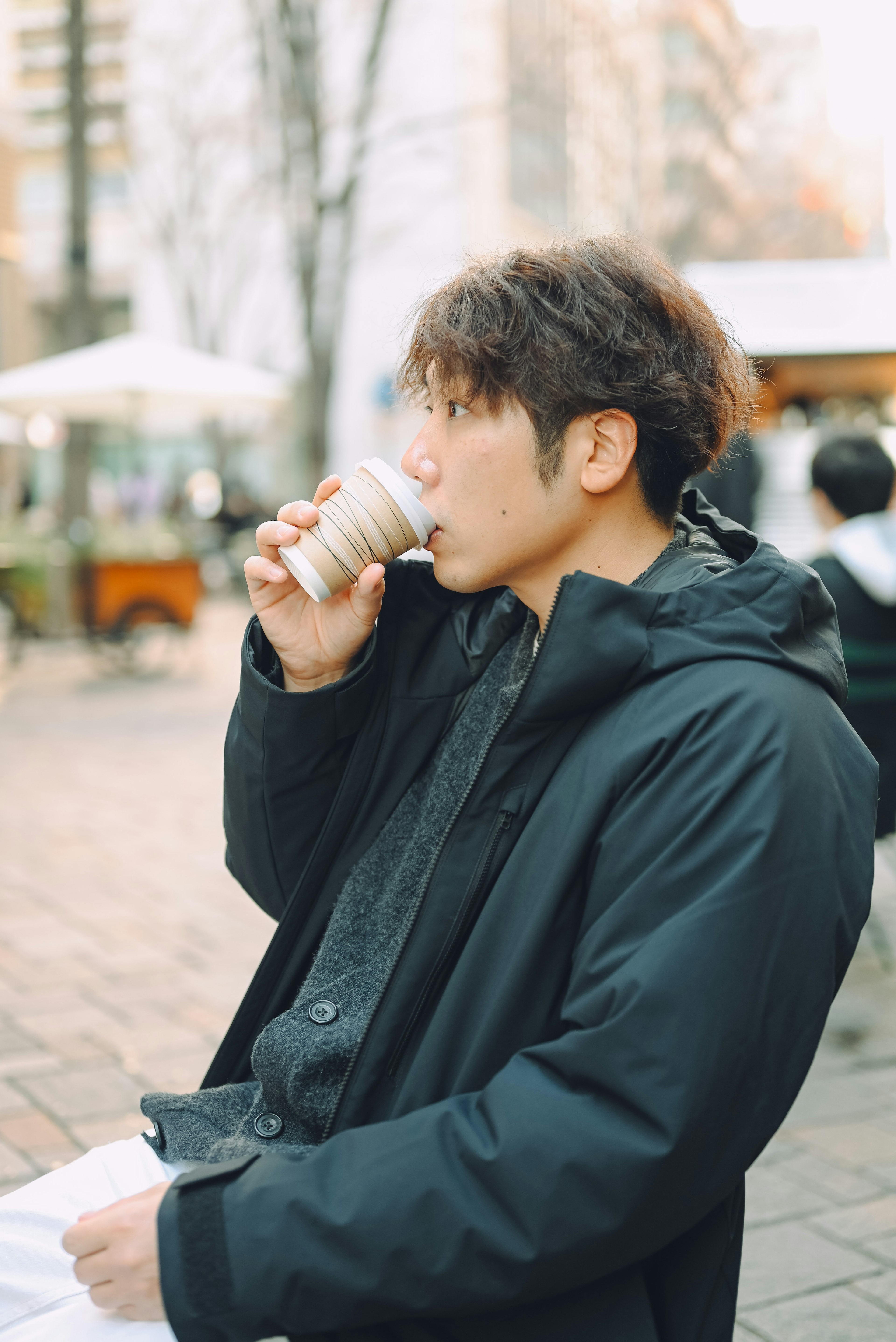 Man drinking from a cup in a cafe wearing a black coat in an urban setting