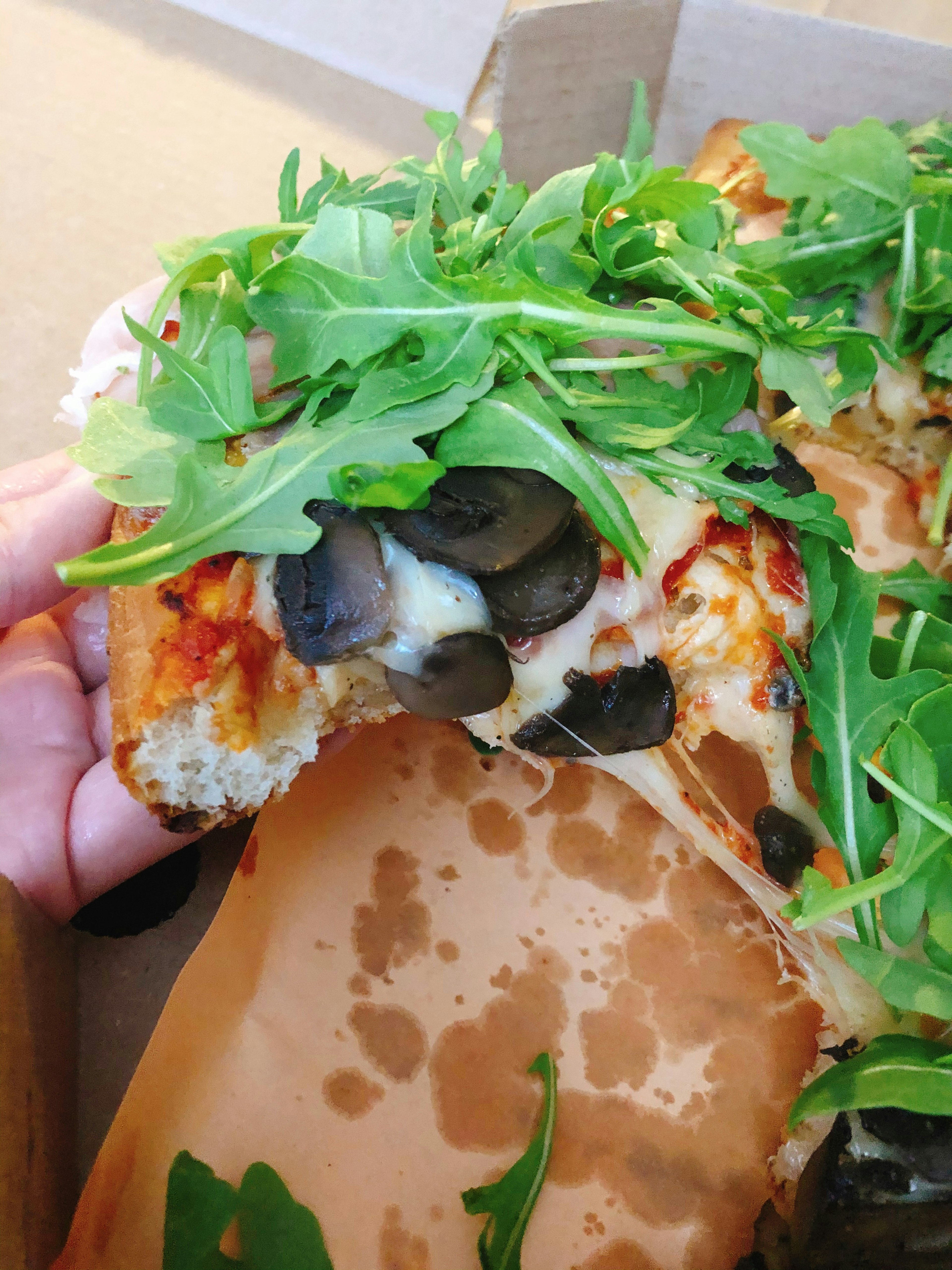 A slice of pizza held in hand topped with olives and arugula