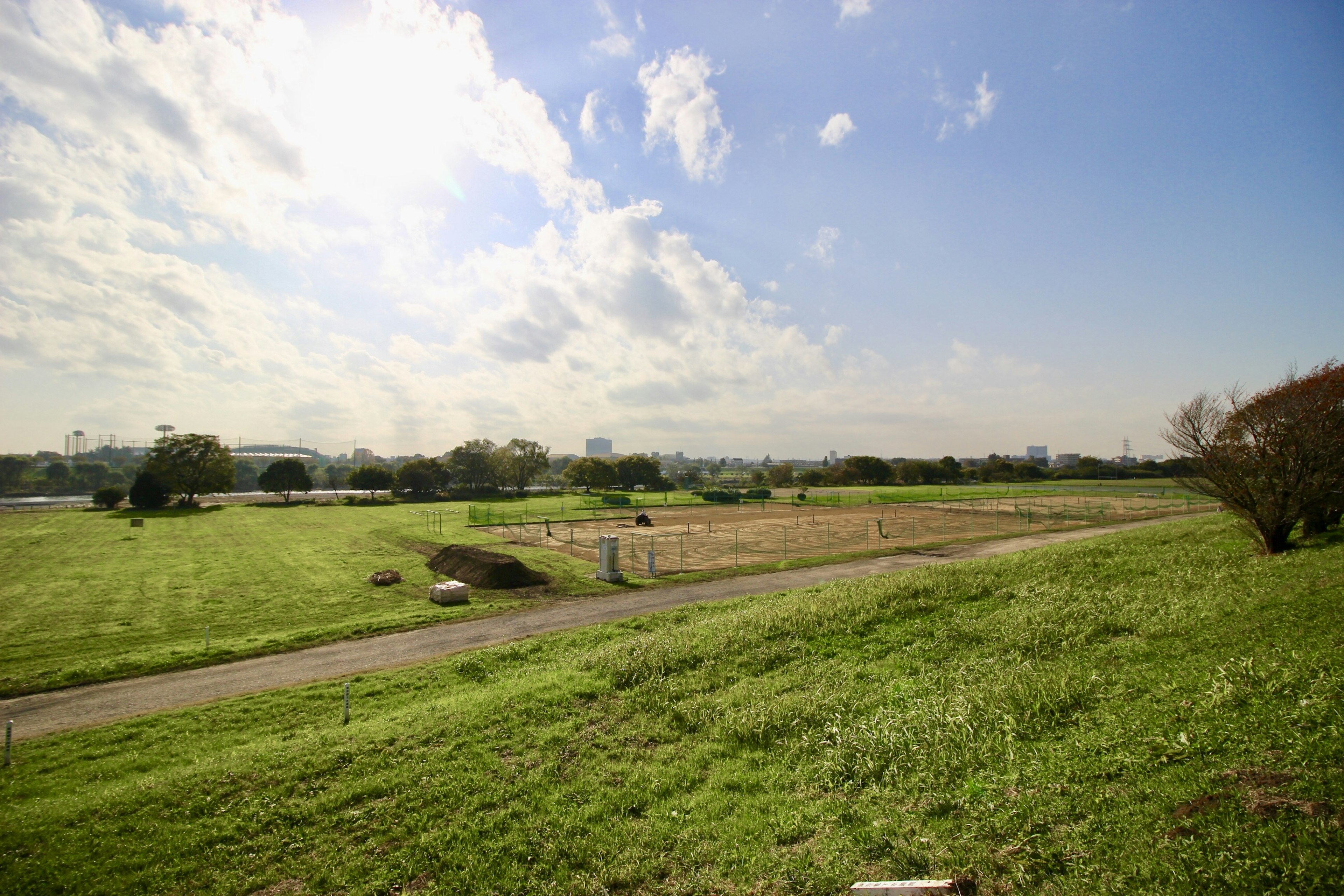 青空と雲が広がる田園風景の写真 緑の草地と遠くの都市のシルエット