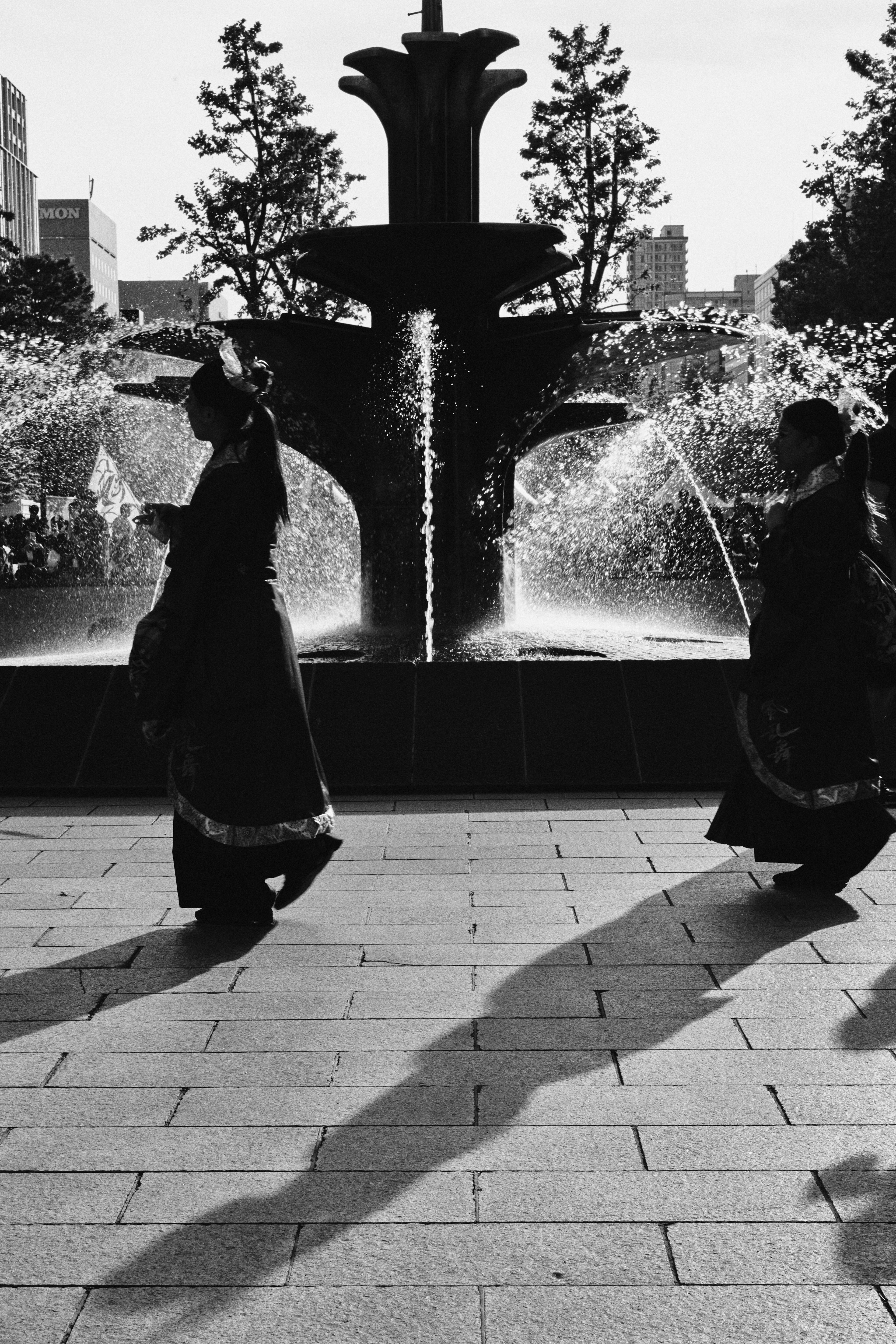 Black and white photo of two figures walking in front of a fountain