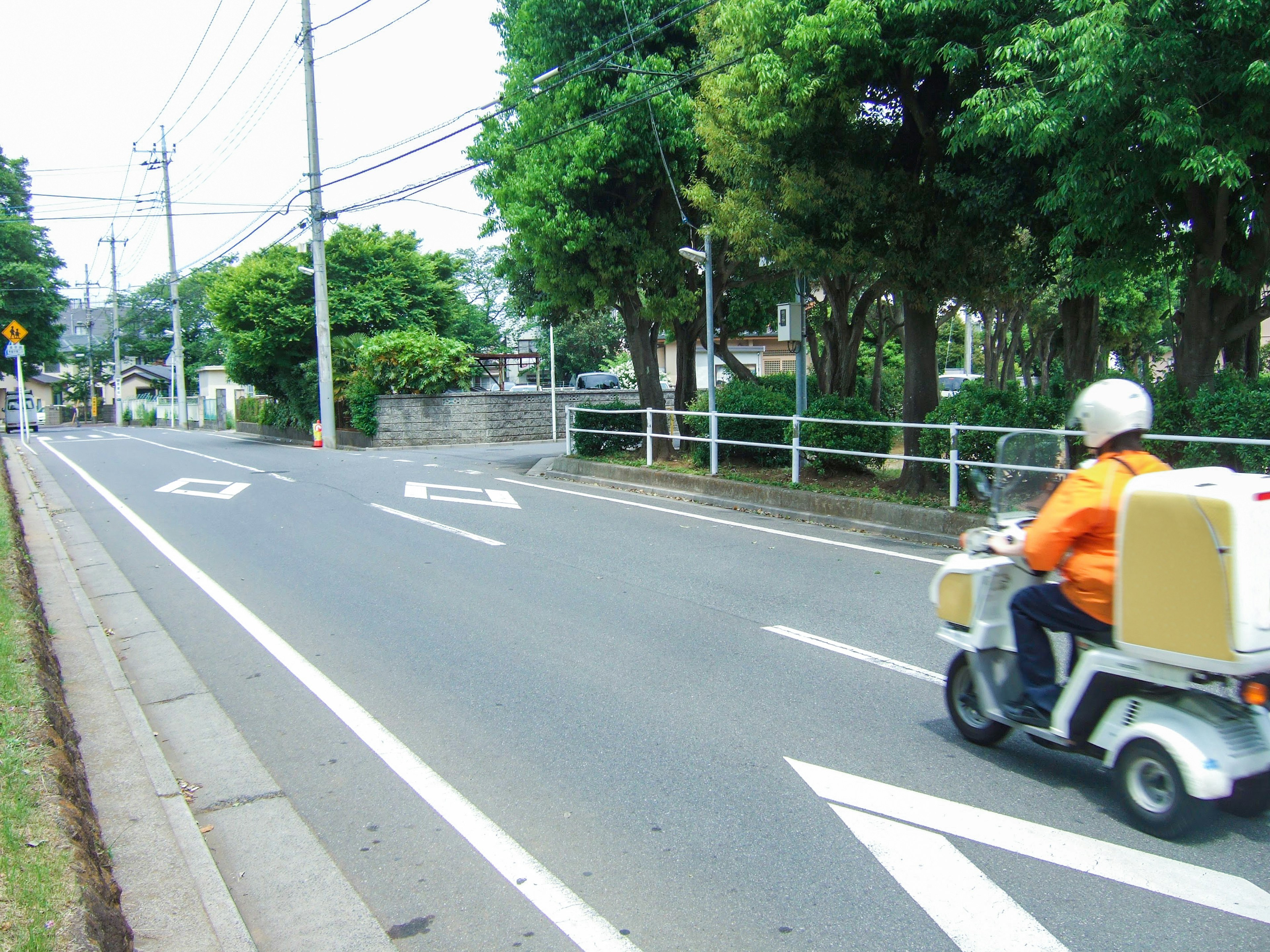 Ein Lieferant in orange Uniform, der auf einem Roller eine Straße fährt