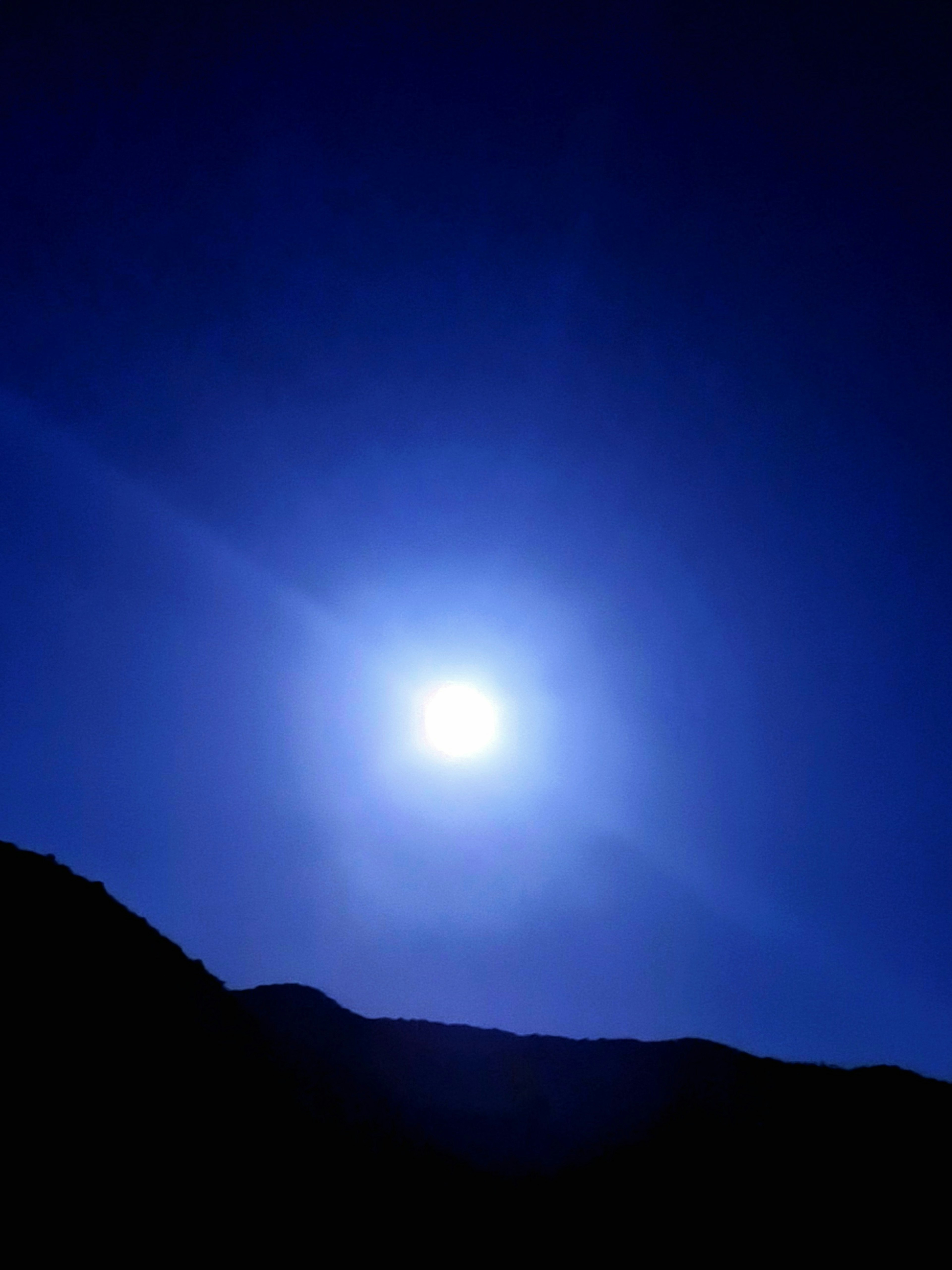 青い空に浮かぶ明るい太陽と山のシルエット