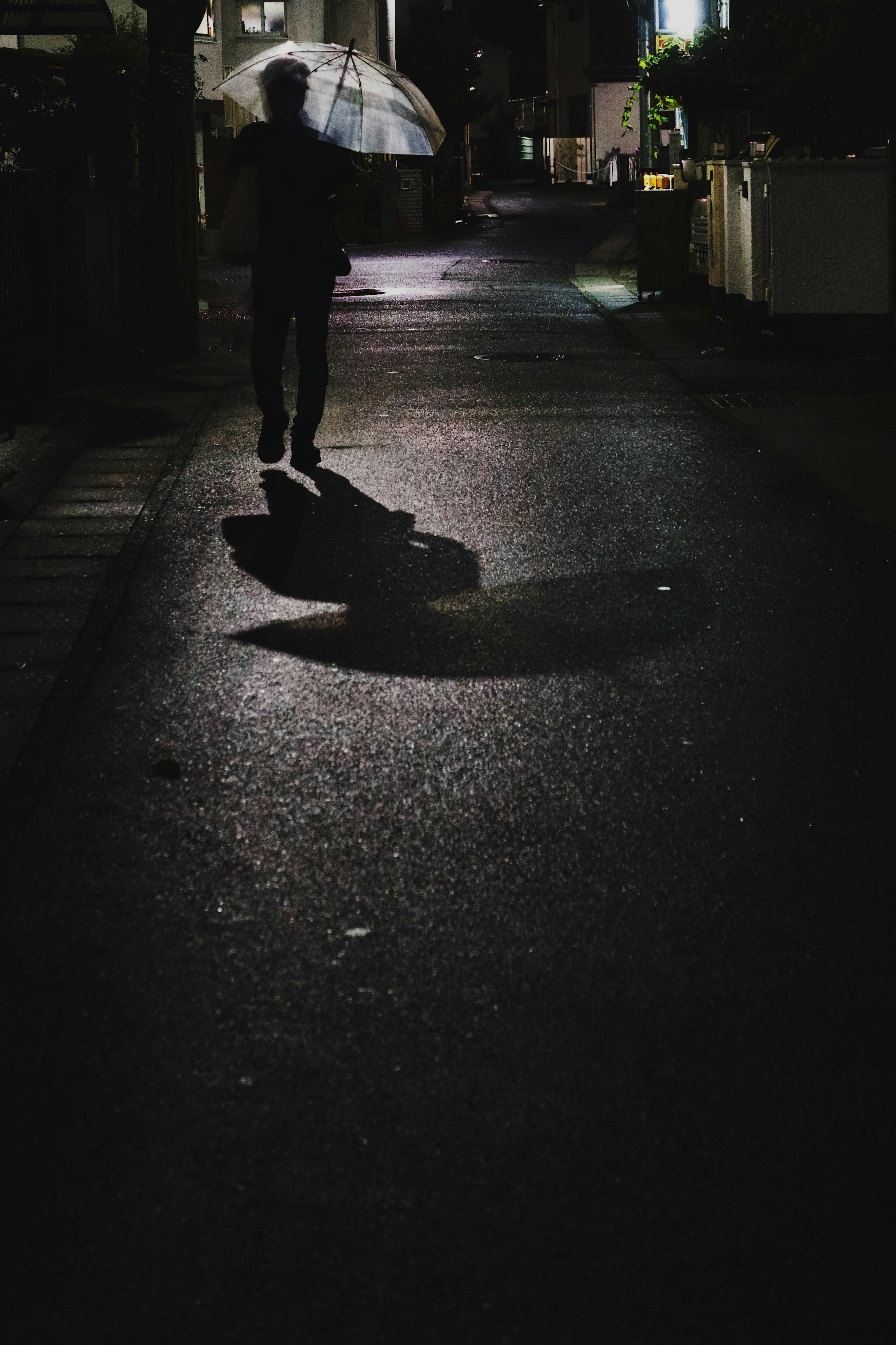 Silhouette d'une personne marchant dans une ruelle sombre tenant un parapluie avec des ombres