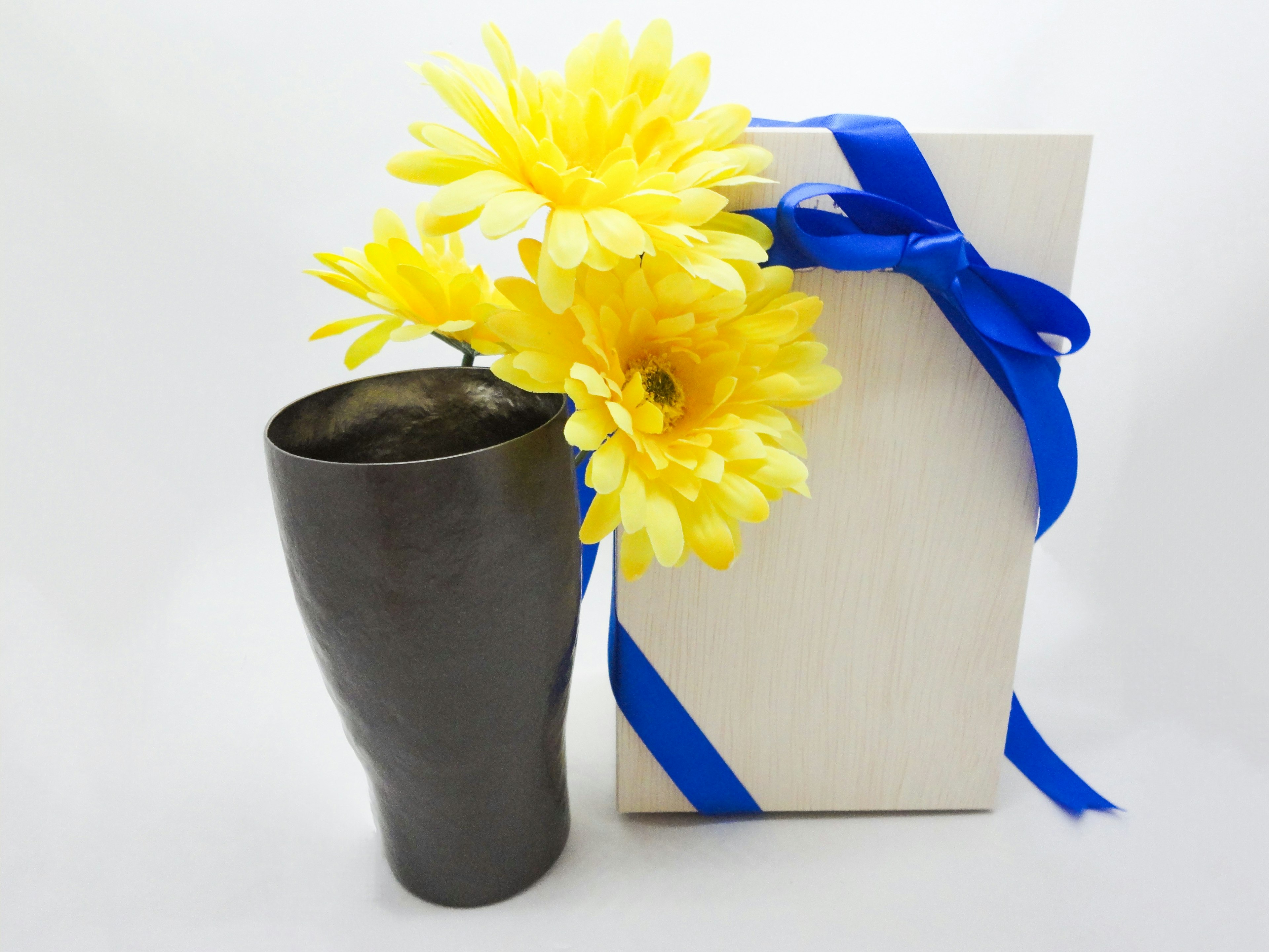 Un vaso nero con fiori gialli accanto a una scatola regalo legata con un nastro blu