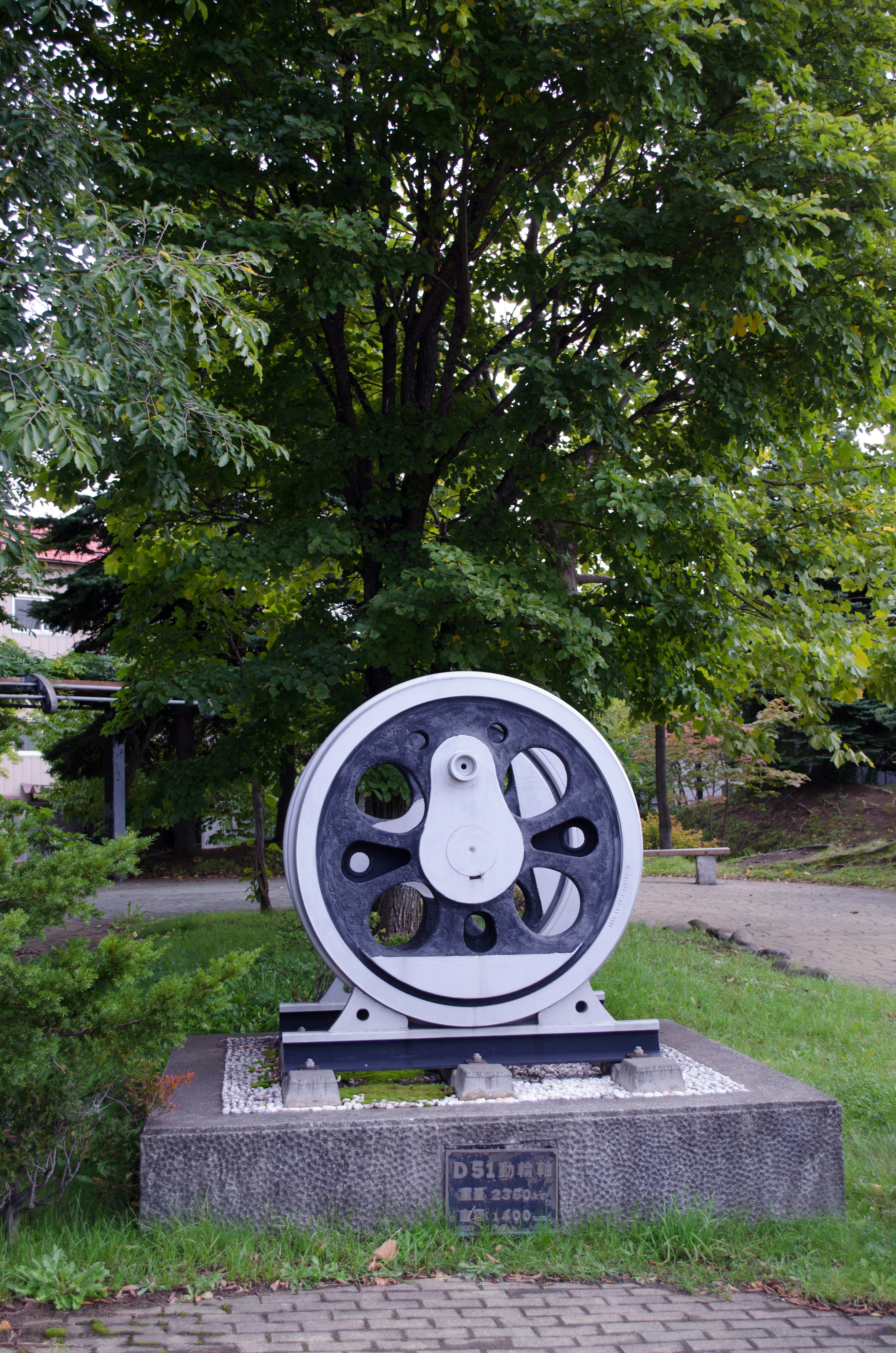 Gran escultura de engranaje negro y blanco en un parque rodeada de árboles verdes