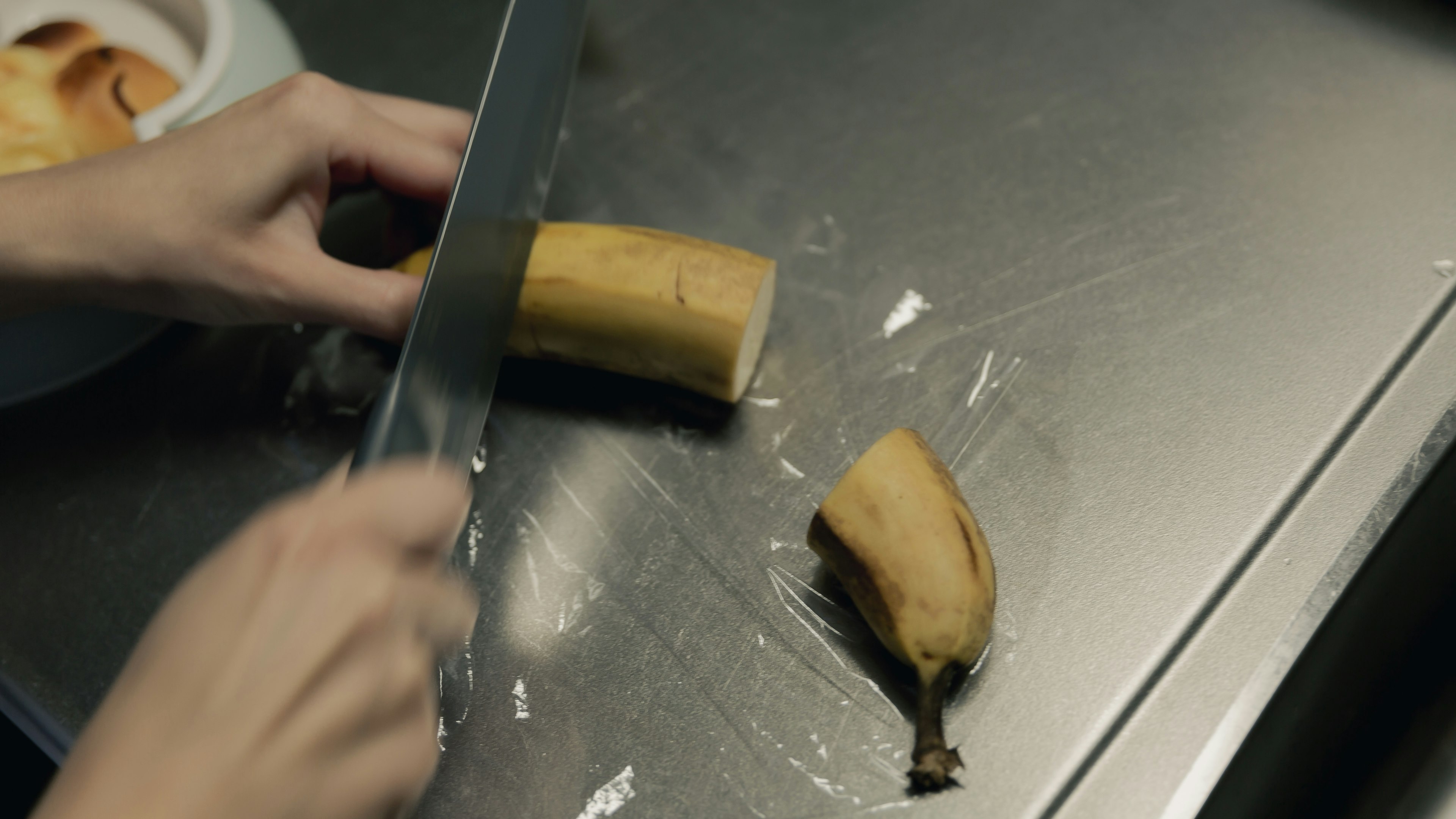 A banana being sliced with a knife and a hand