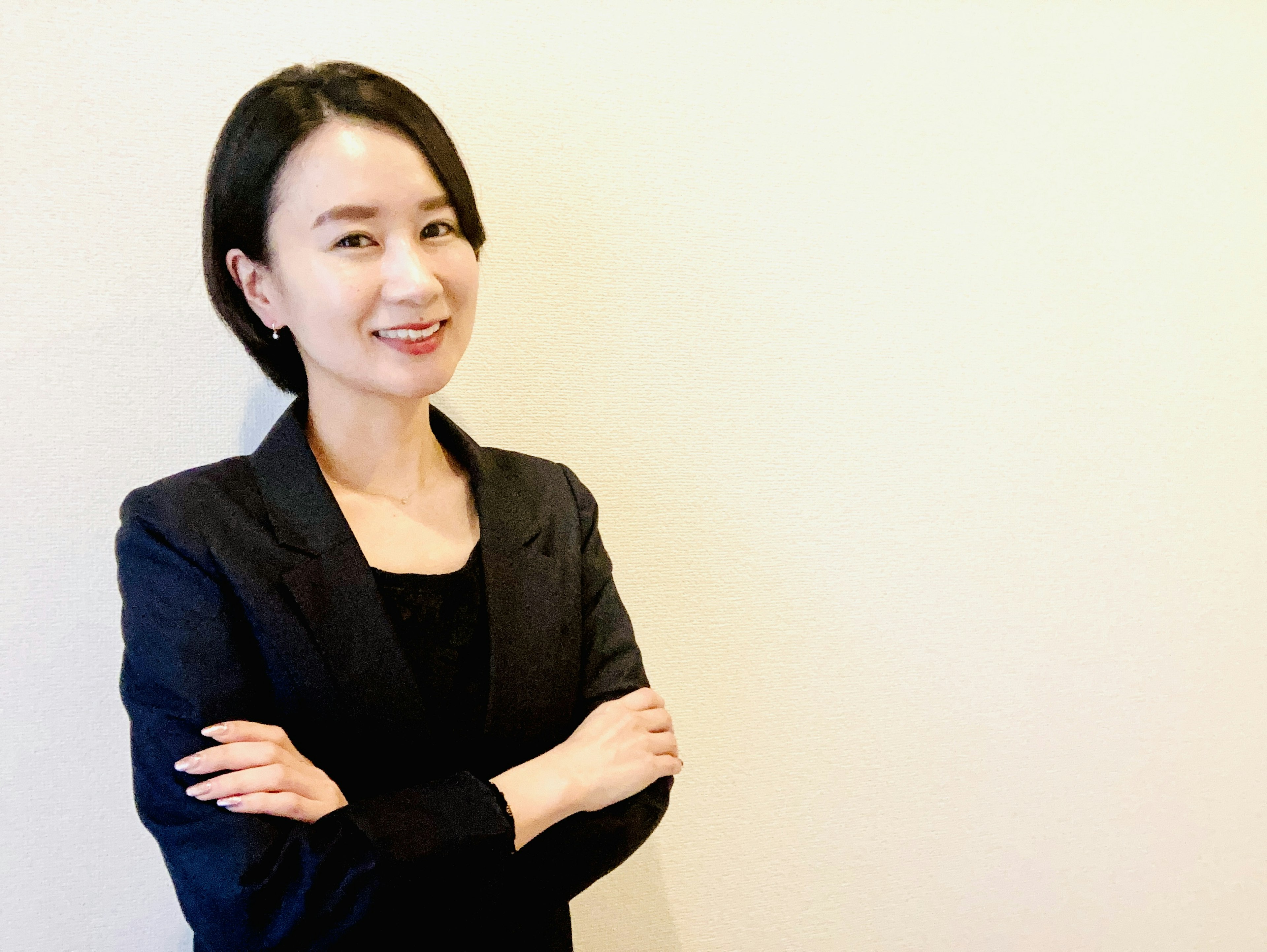 A woman in a business suit smiling with her arms crossed