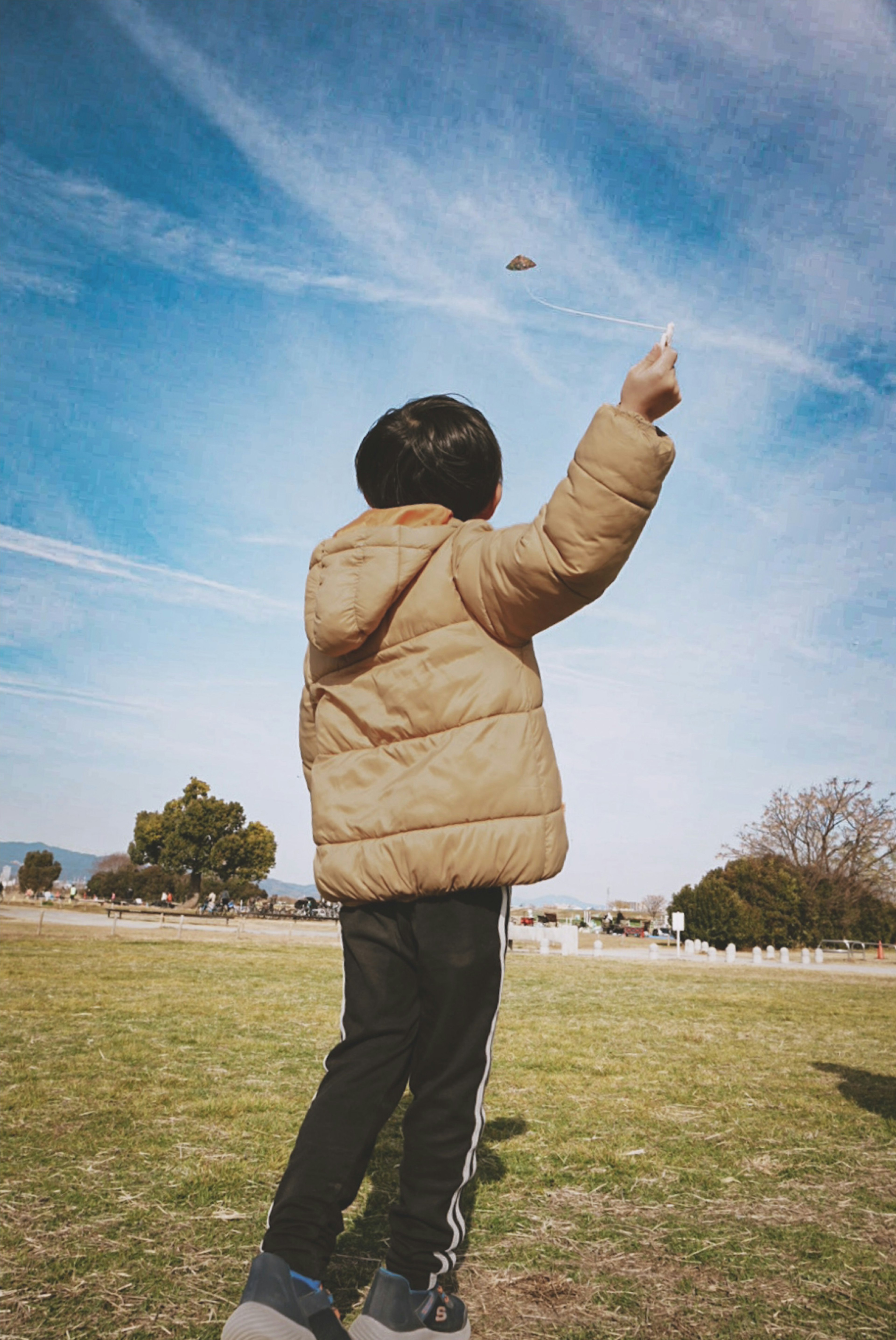 Child in a puffy jacket pointing at the sky in a park