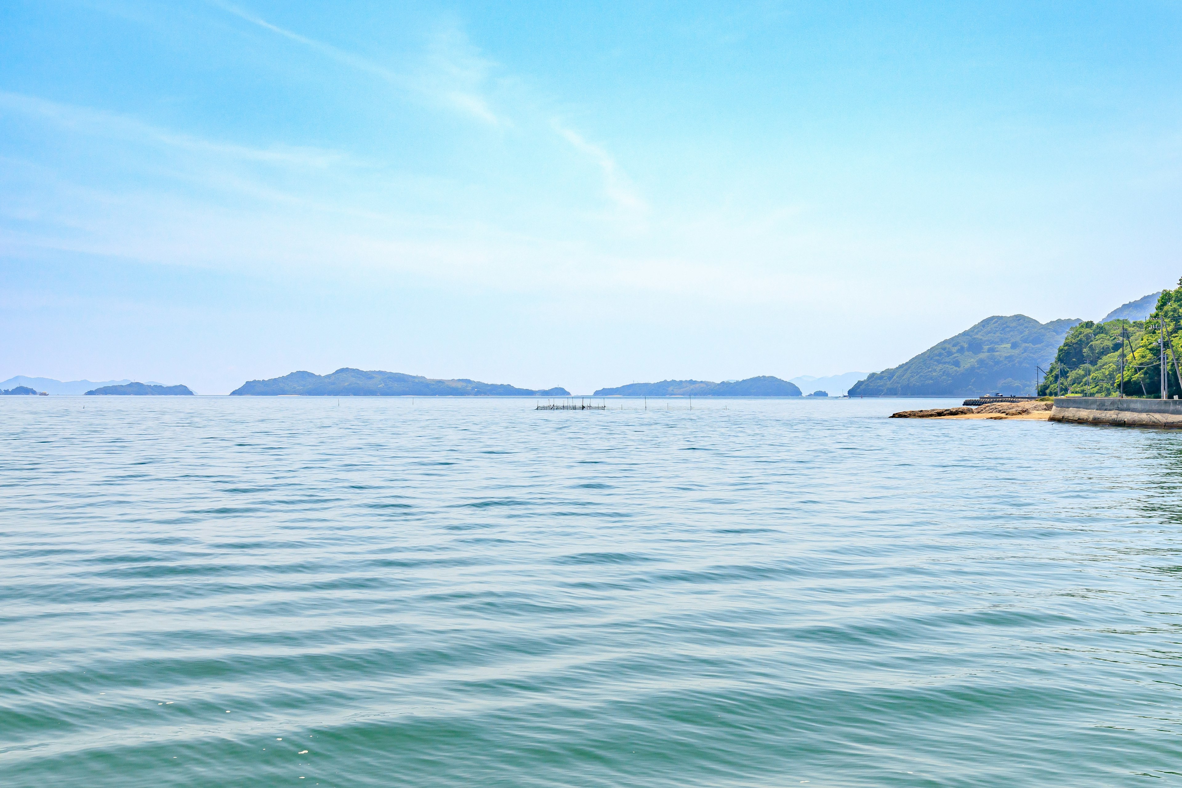 Pemandangan laut tenang dengan langit biru dan pulau-pulau jauh