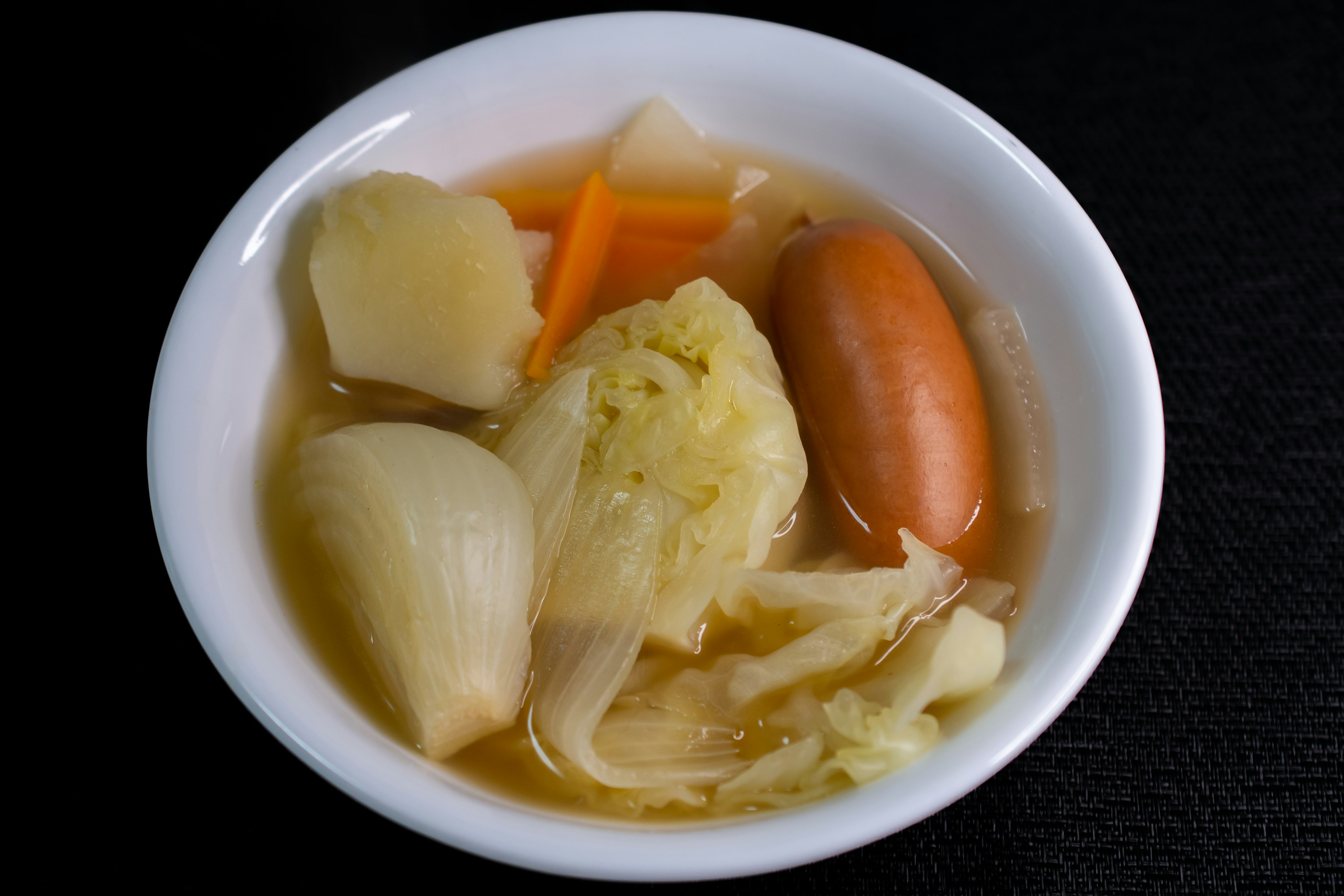 A bowl of soup with various vegetables including cabbage carrots and sausage