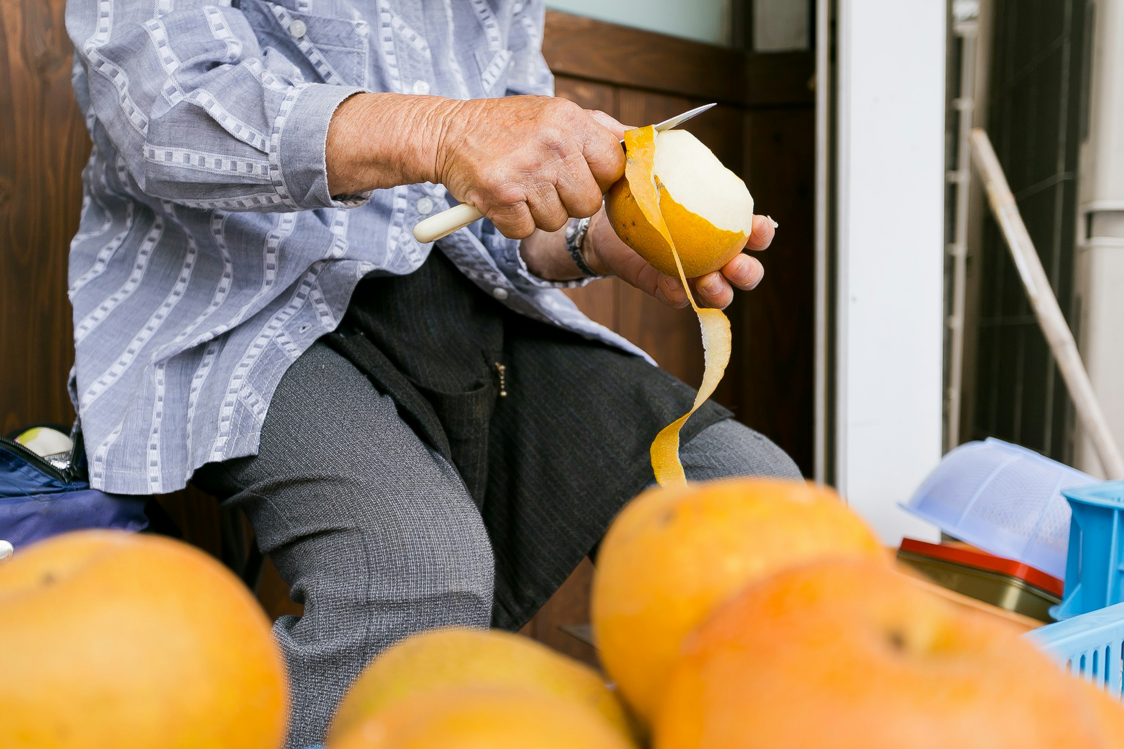 Nahaufnahme von Händen, die eine Orange schälen, mit mehreren Orangen im Vordergrund