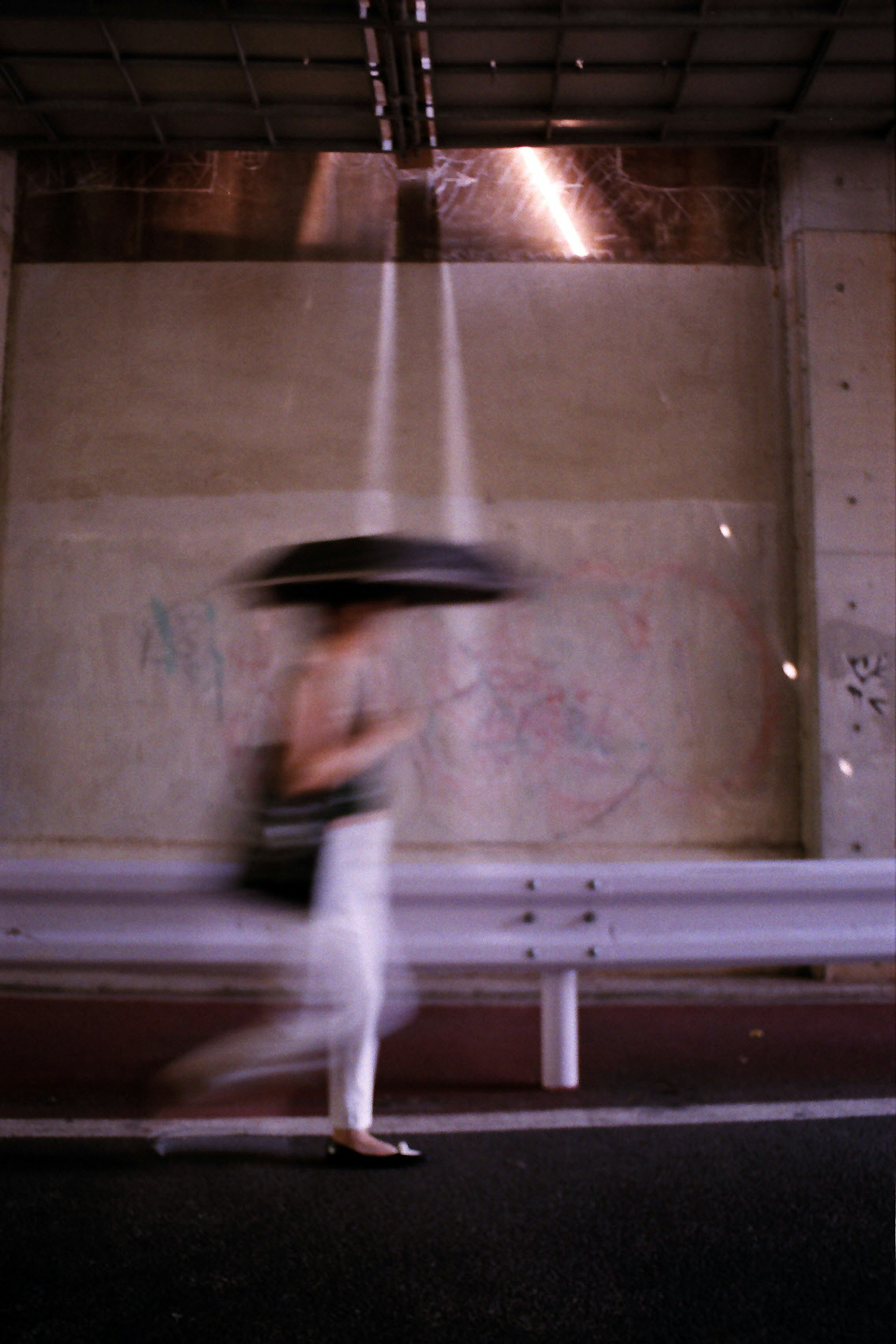 A person holding a moving umbrella walking against a modern backdrop