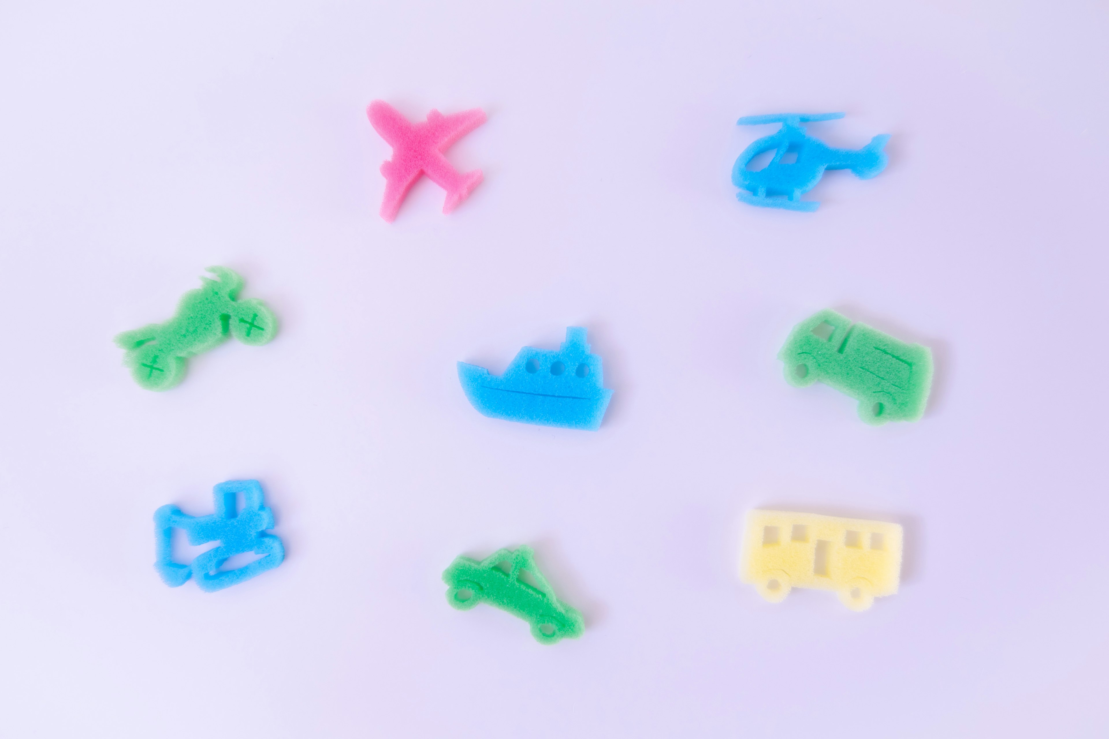 Petits jouets en plastique colorés en forme de véhicules éparpillés sur un fond blanc