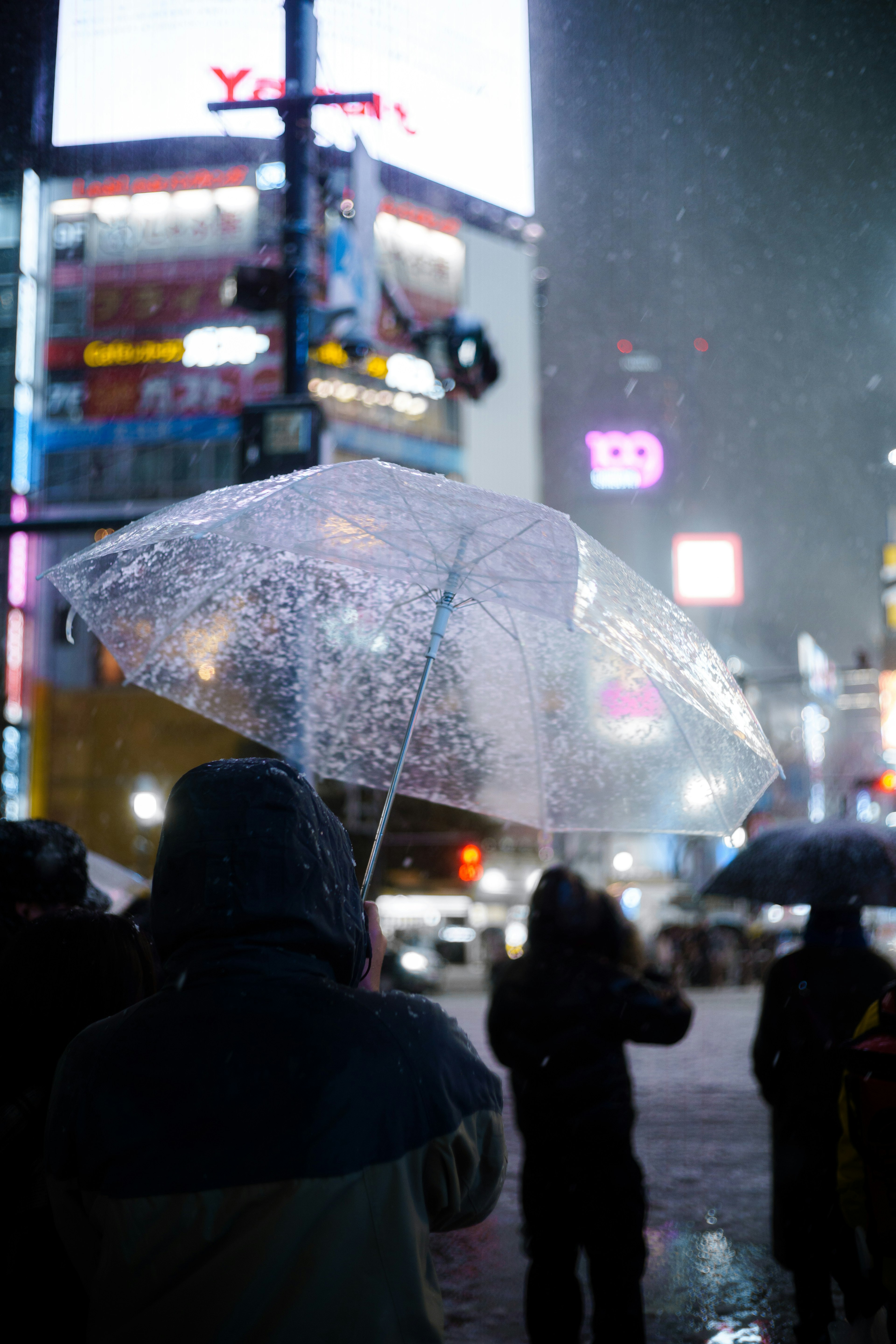 夜の雪の中で透明な傘を持つ人々のシルエットと煌めくネオン