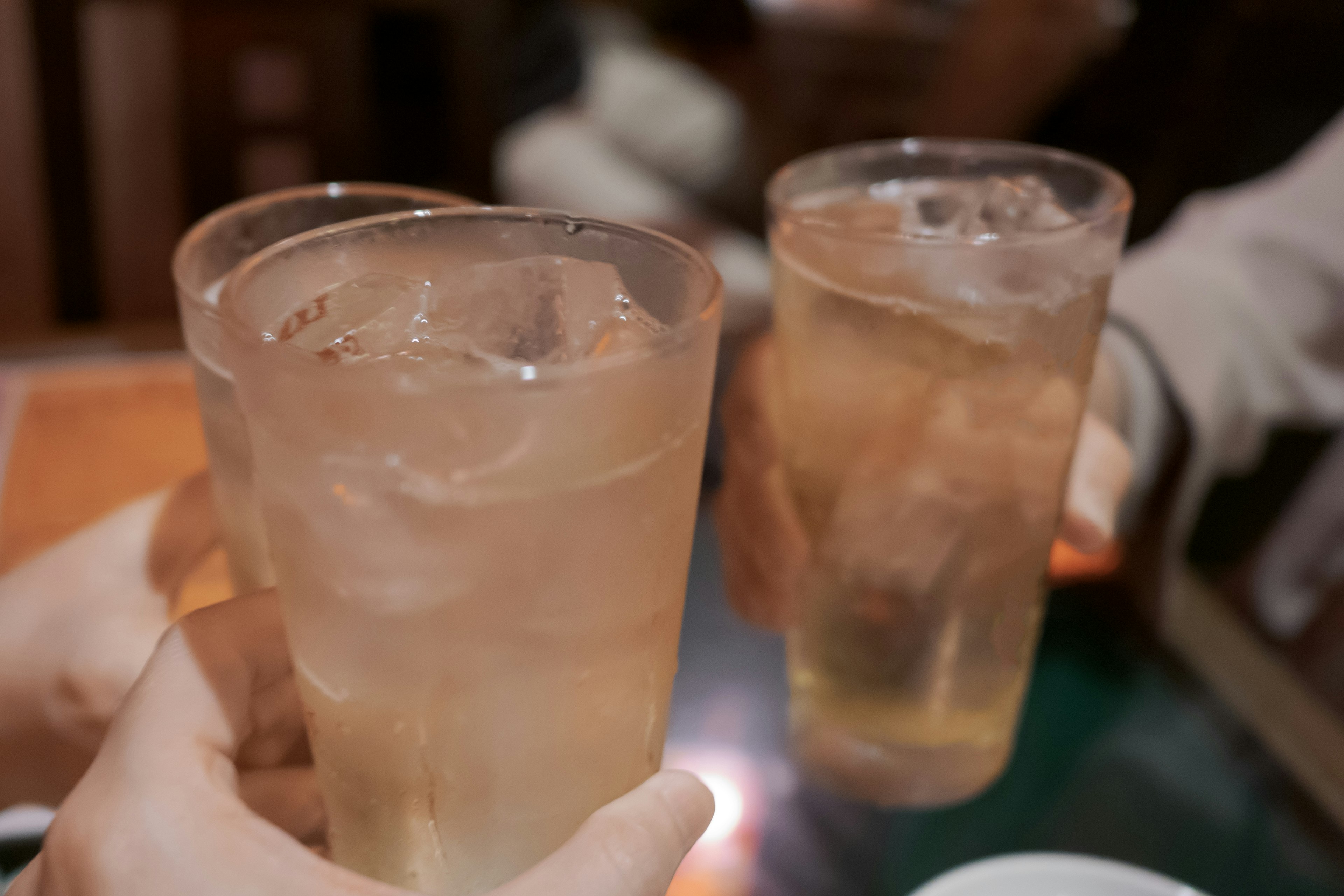 Close-up of hands holding glasses for a toast with ice-filled drinks