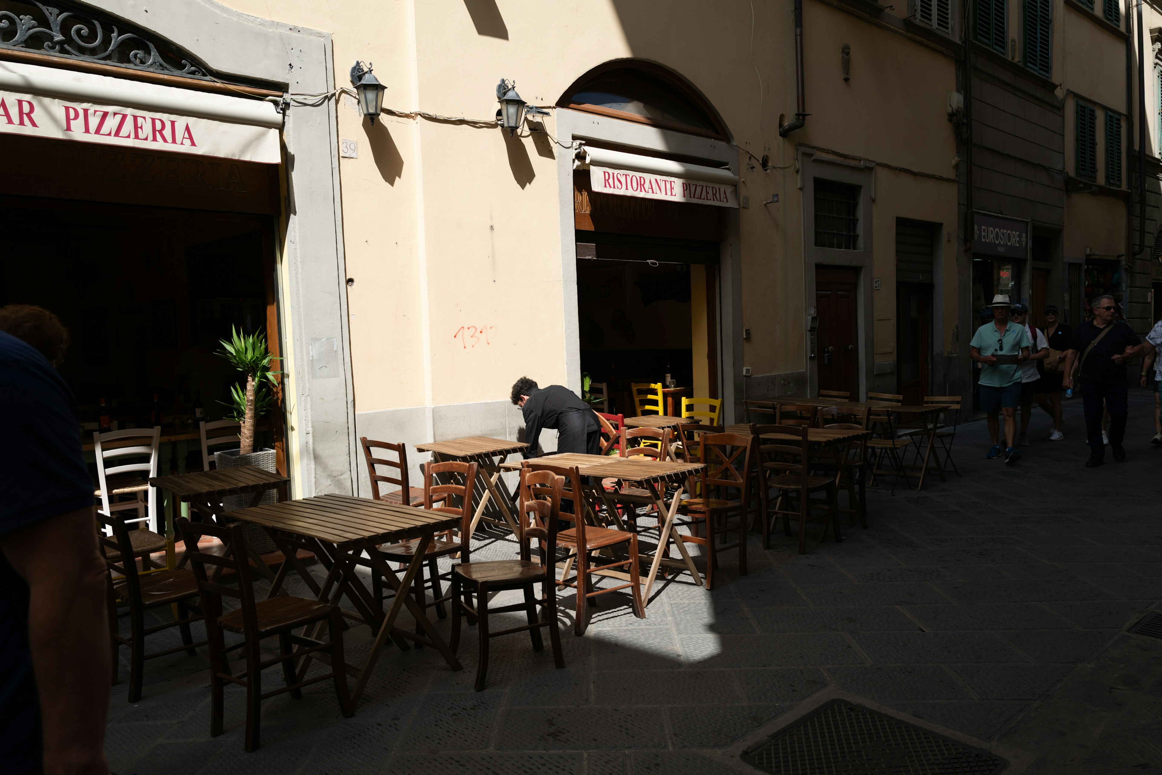 Außensitz einer Pizzeria mit Holztischen in einer engen Straße