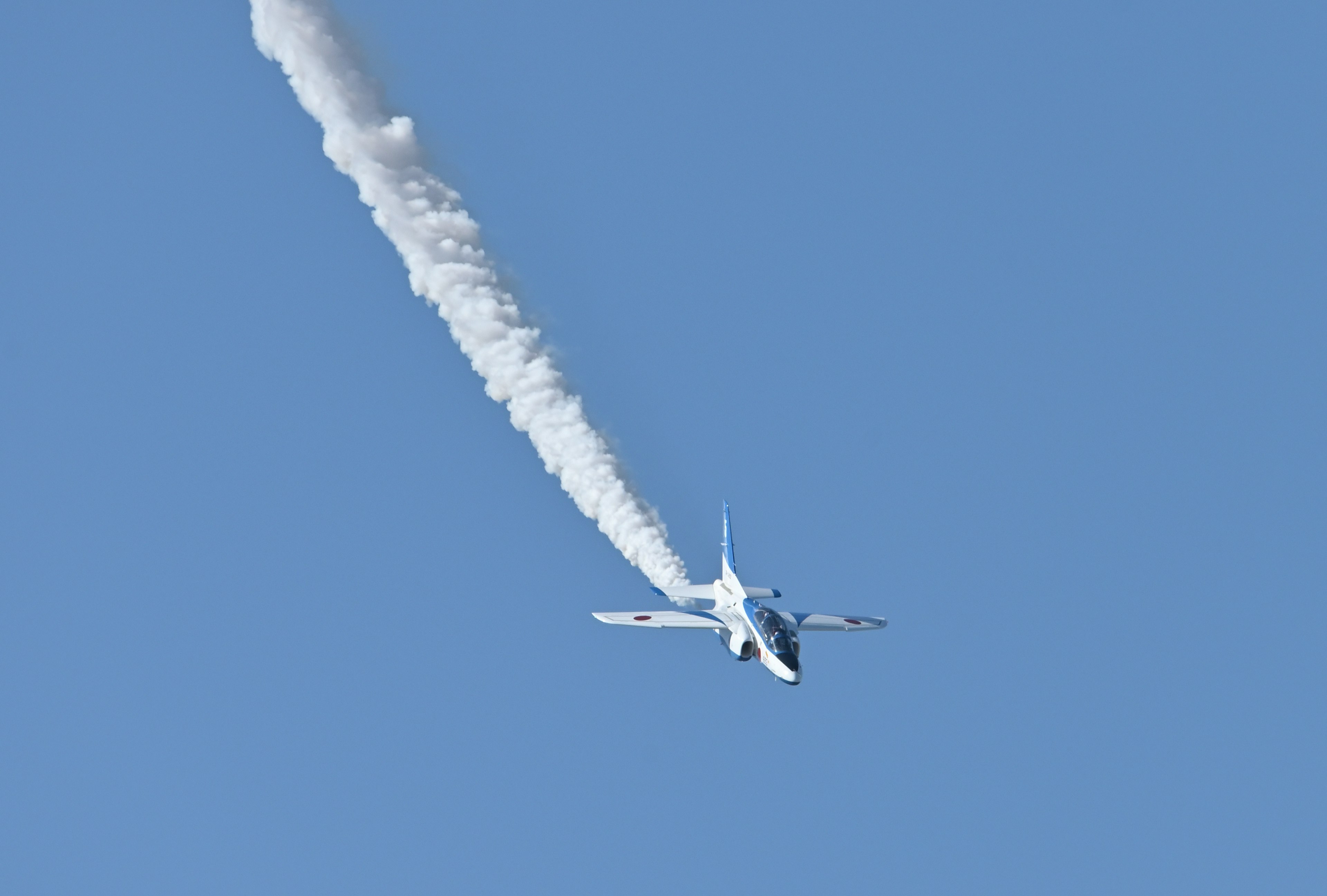 An airplane flying against a blue sky with a white contrail trailing behind