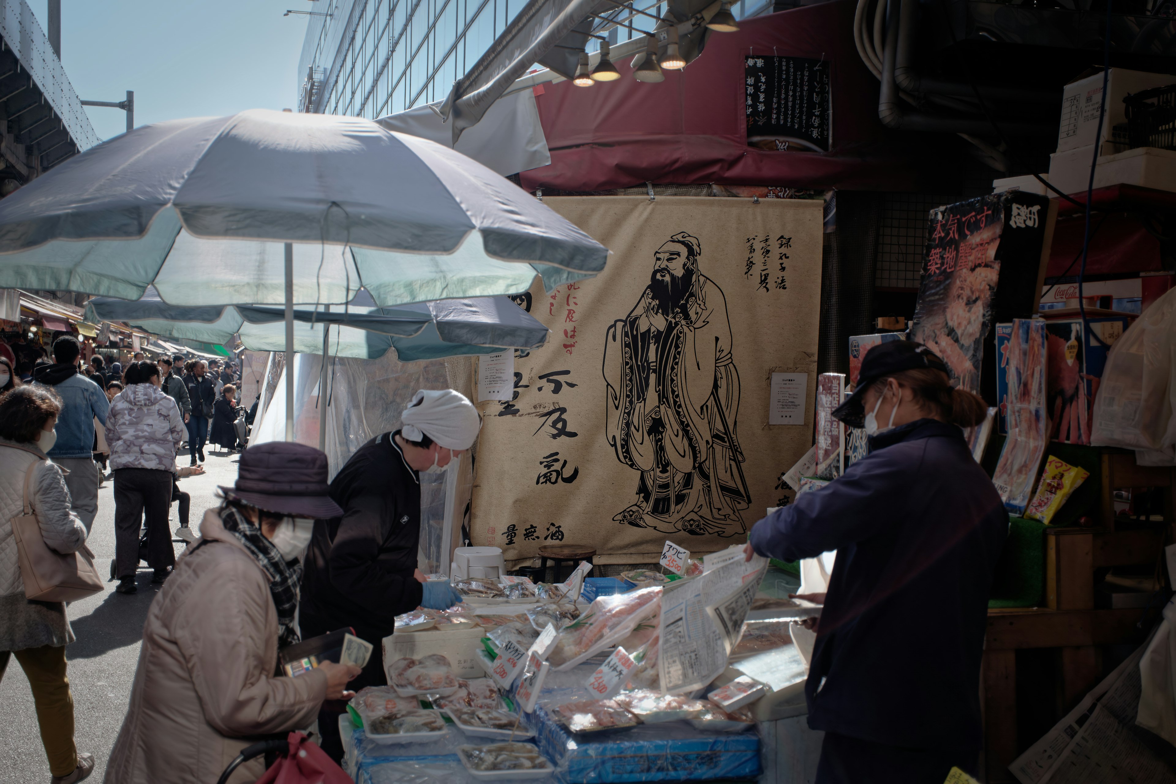 People selecting food at a street stall under an umbrella