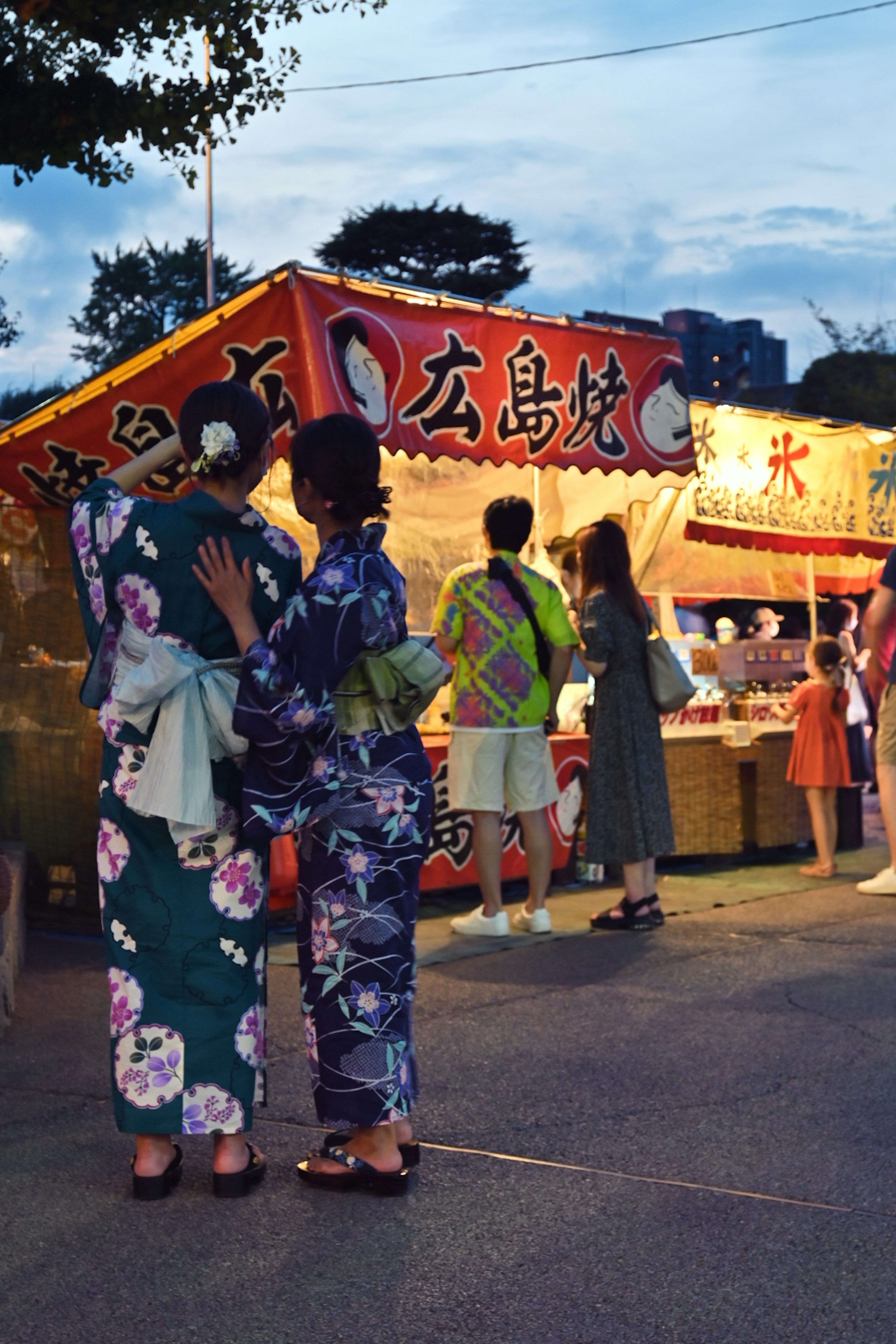 Wanita berpakaian kimono di festival musim panas di depan stan makanan