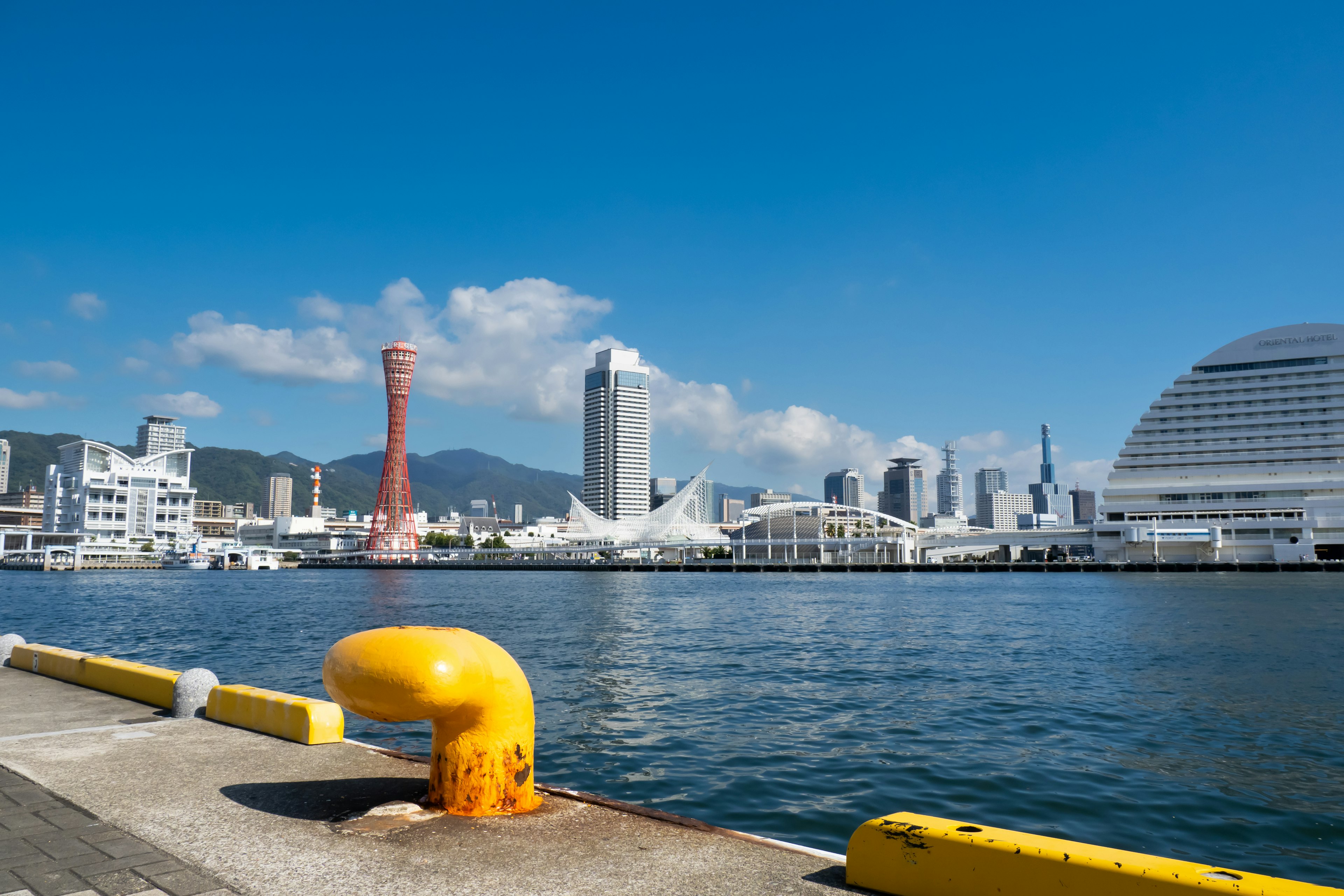 Pemandangan pelabuhan Kobe dengan bollard kuning dan gedung pencakar langit