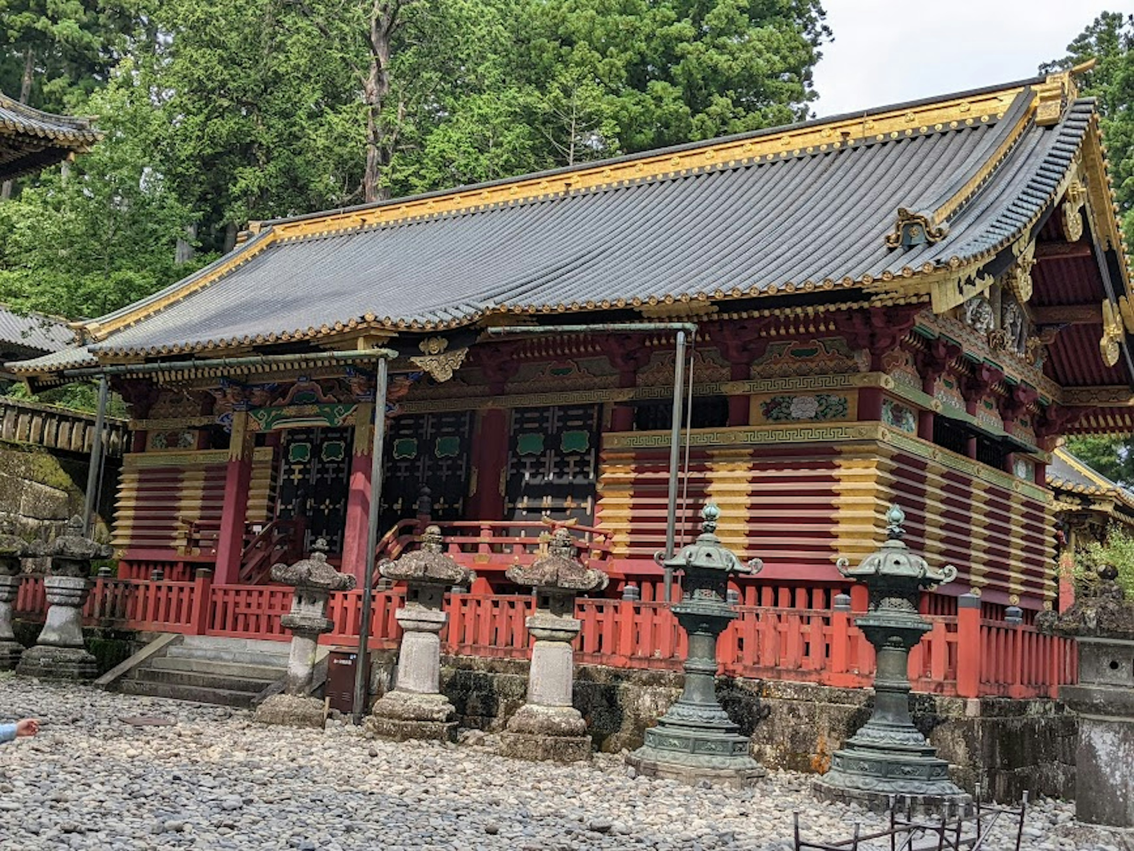 Beautiful Japanese shrine building with red and gold decorations surrounded by greenery and stone lanterns