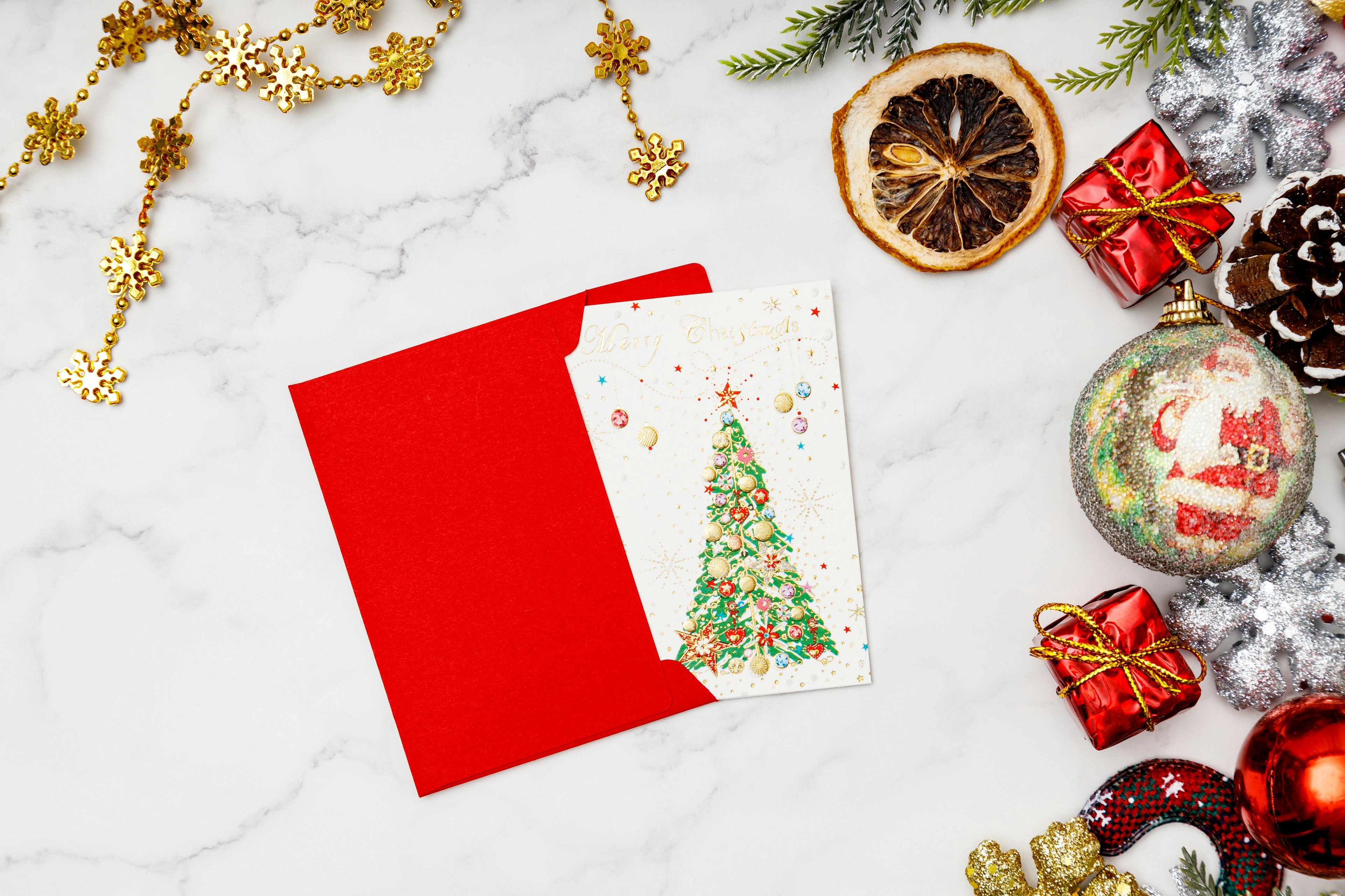 Sobre rojo con una tarjeta de Navidad sobre una mesa de mármol rodeada de decoraciones festivas