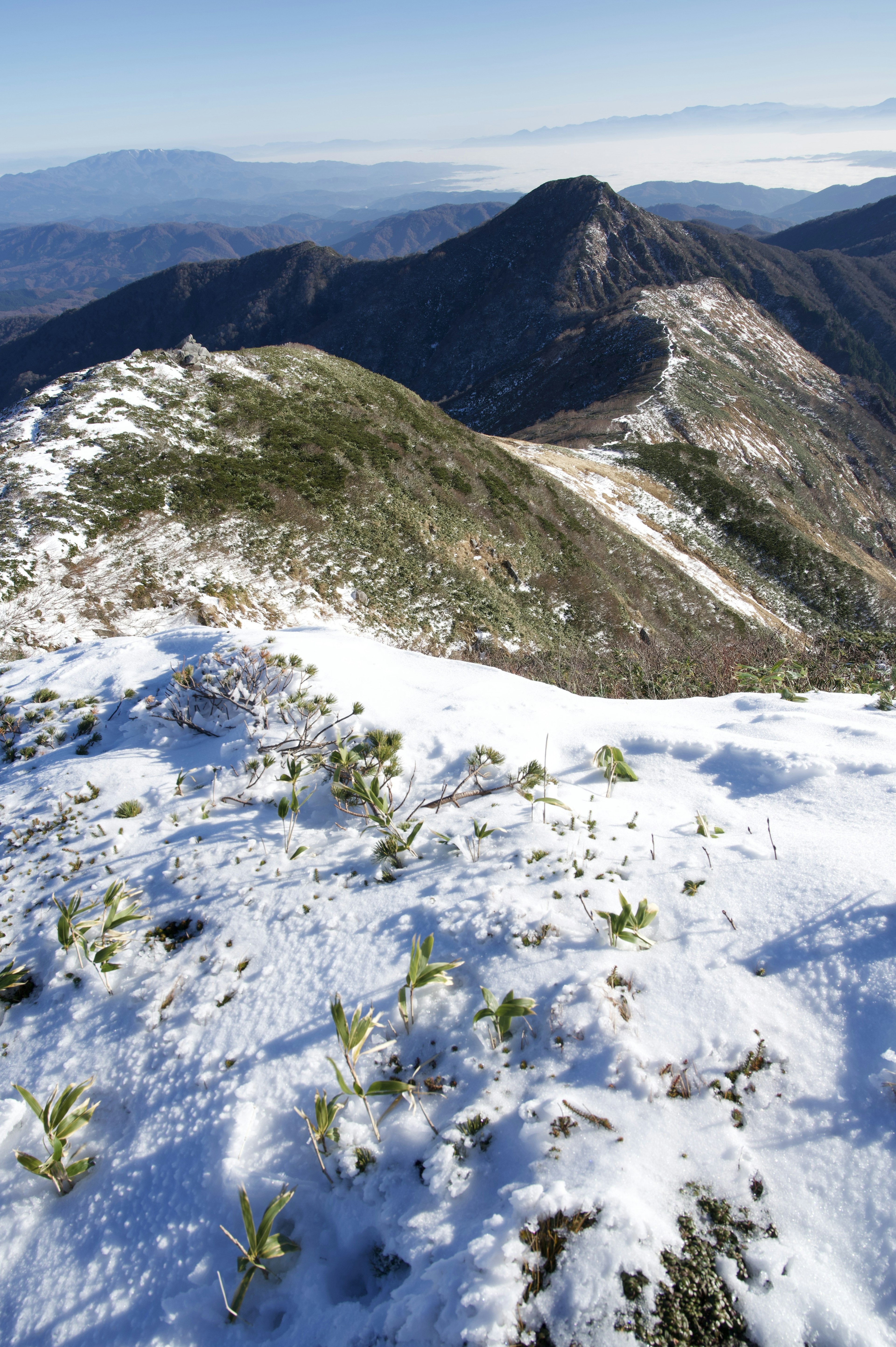 雪に覆われた山の頂上からの風景 緑の草と遠くの山々が見える