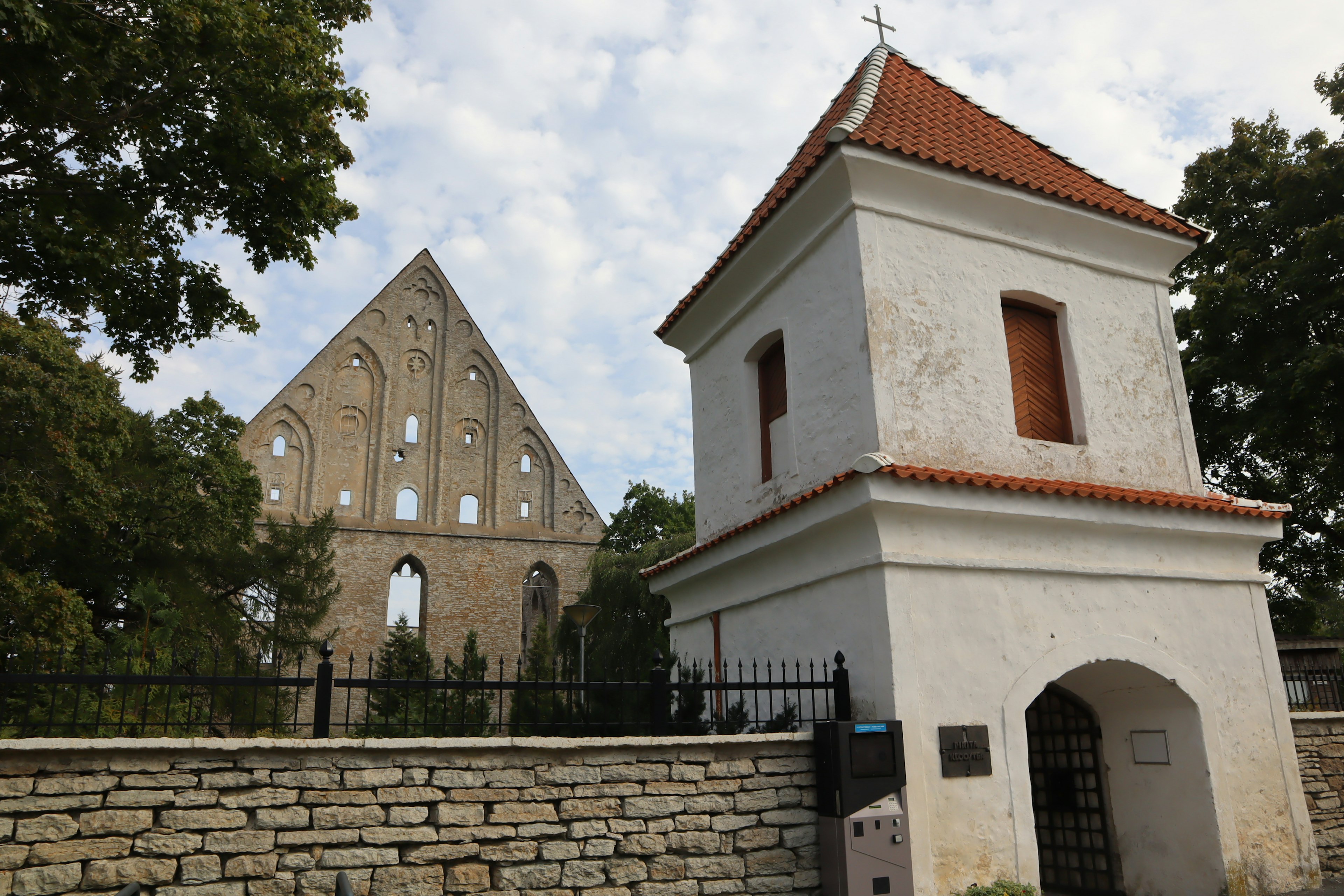 A white building with a red roof next to the ruins of a church