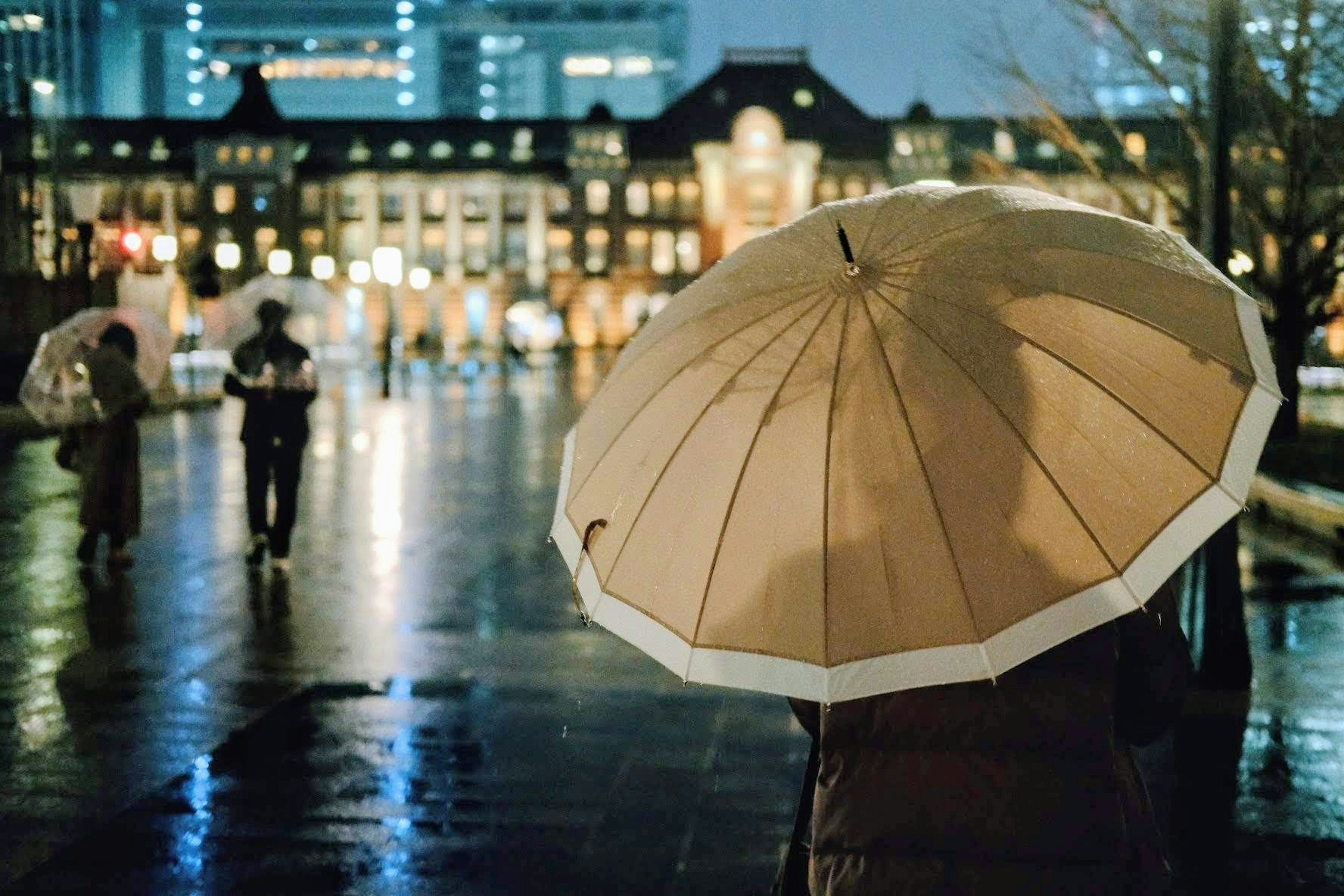 Person mit einem Regenschirm in einer nächtlichen Stadtlandschaft mit beleuchteten Gebäuden