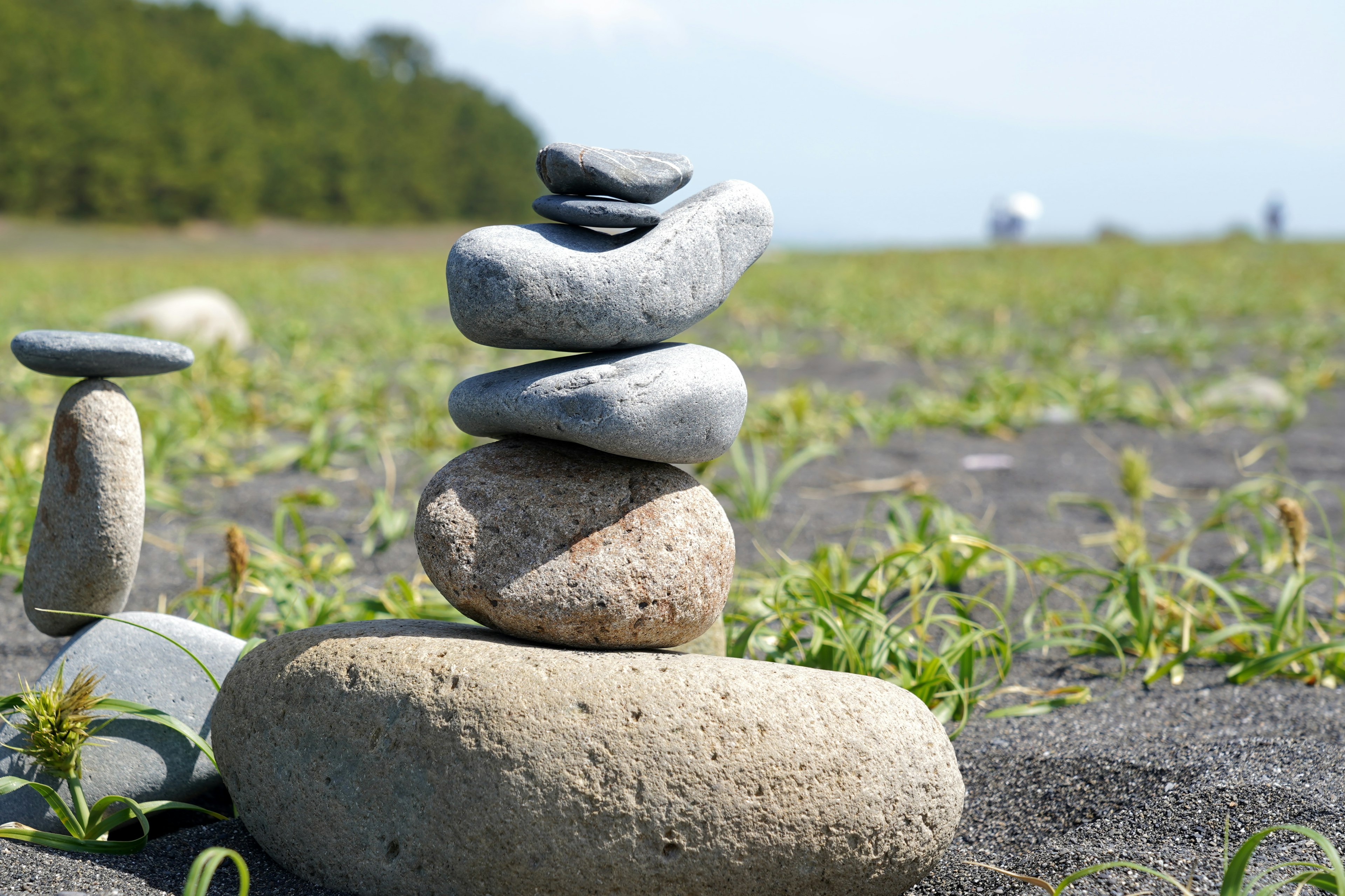 A stack of smooth stones on a sandy beach with green grass in the background