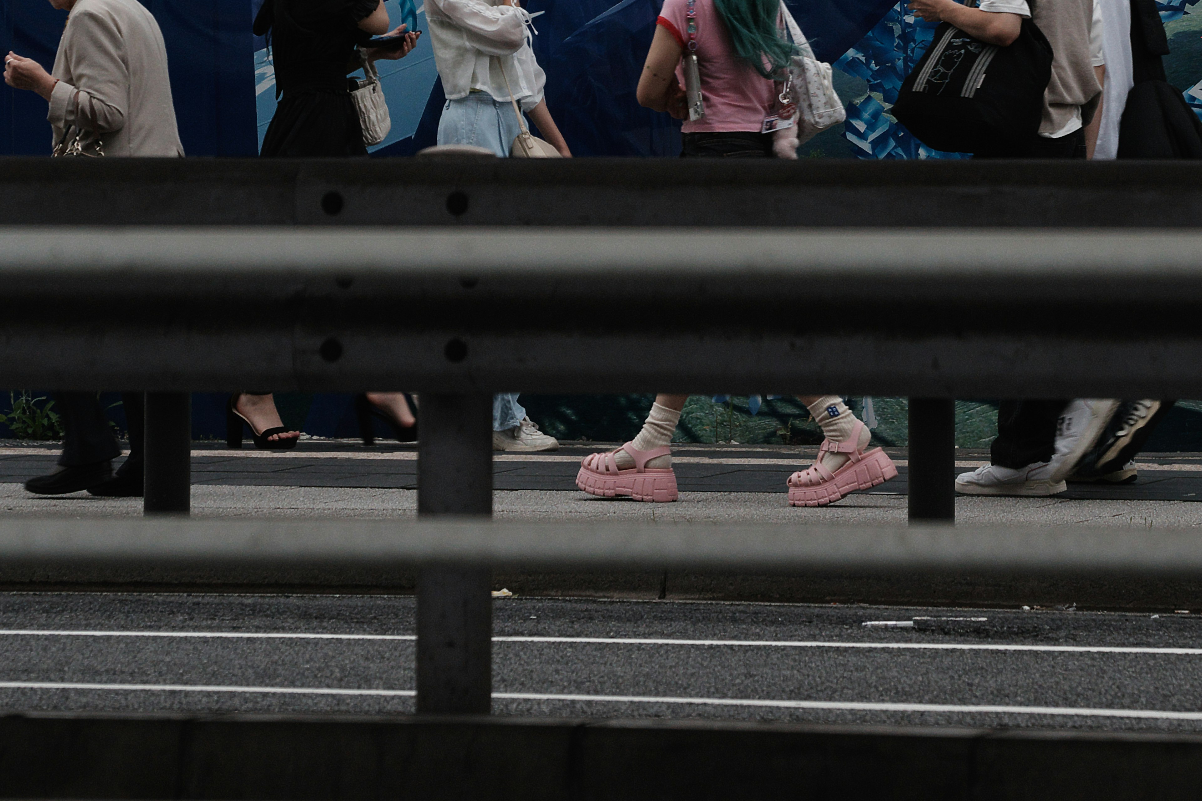 Una scena di strada con persone che camminano visibili dietro una barriera con scarpe rosa