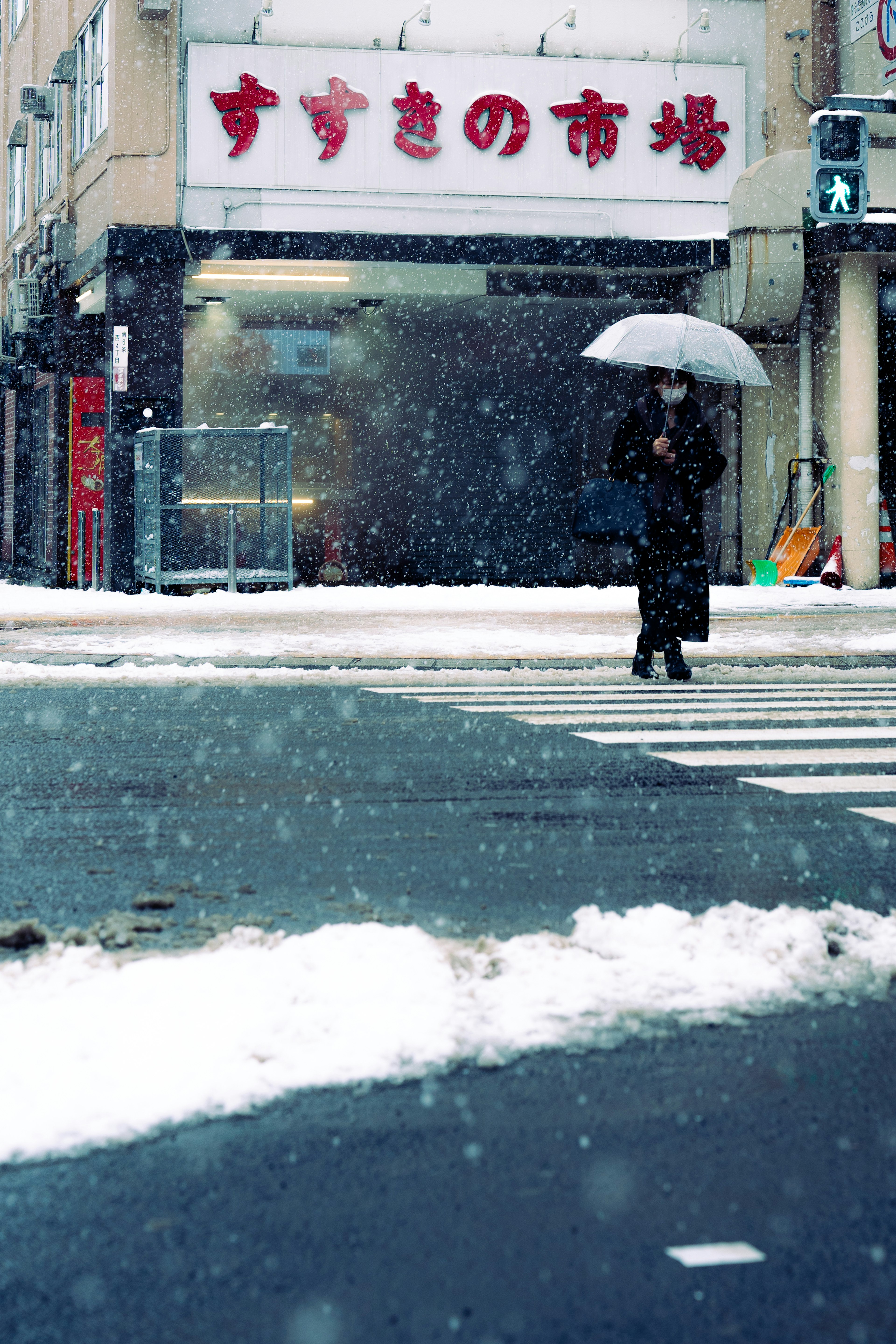 Eine Person, die mit einem Regenschirm im Schnee am Zebrastreifen geht