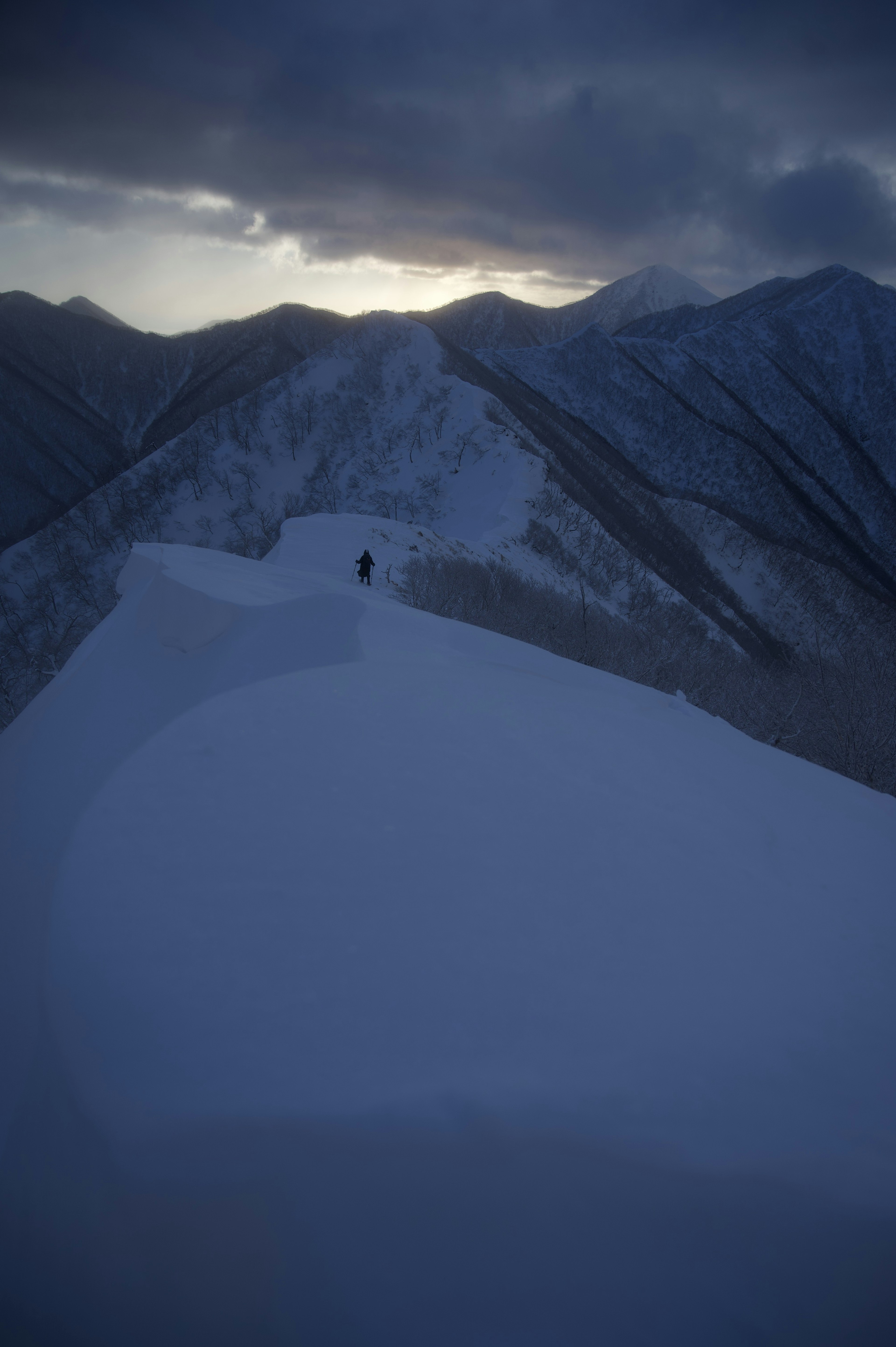 雪に覆われた山の稜線に一人の登山者が立っている風景