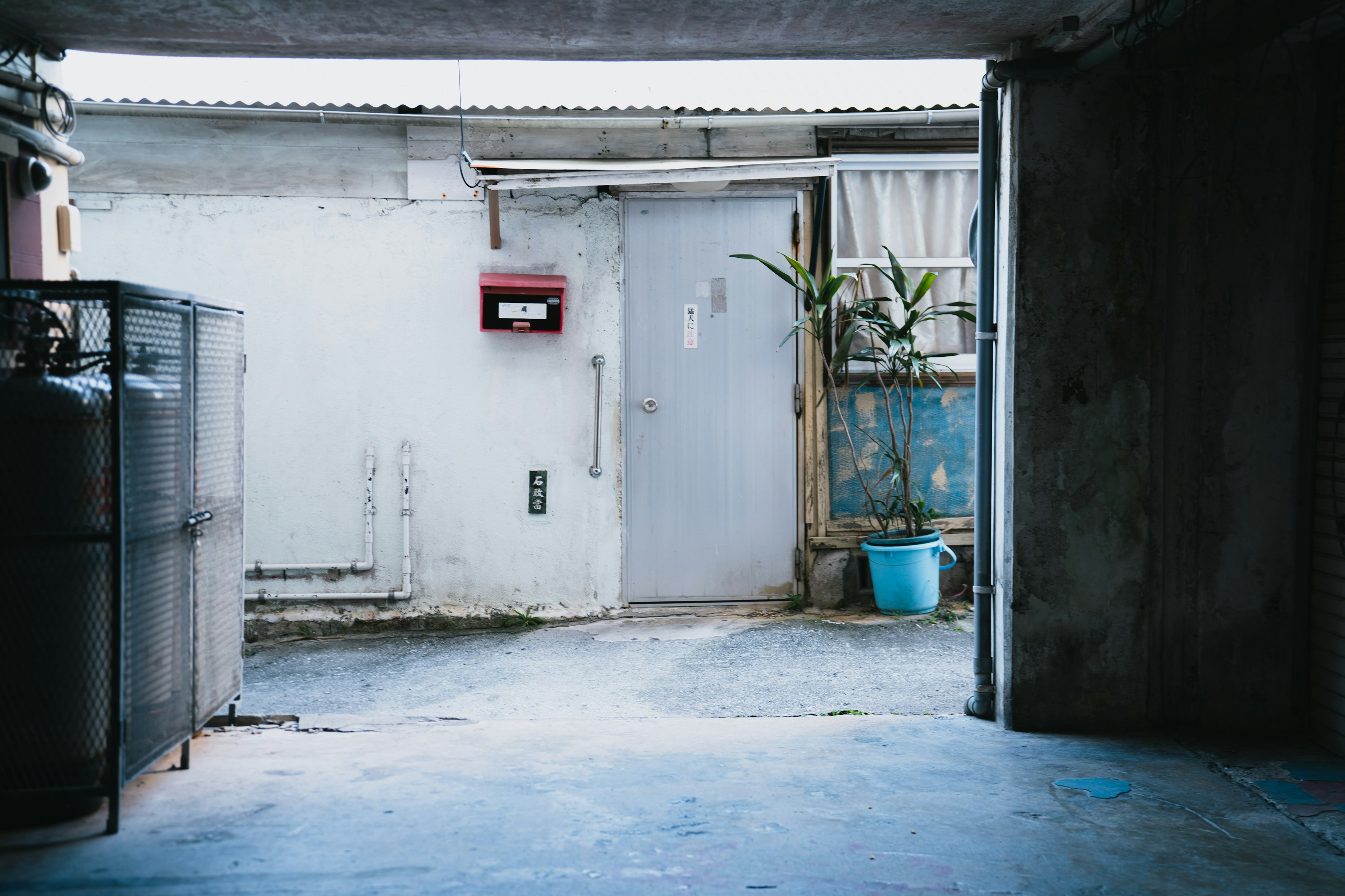 Lorong redup yang mengarah ke pintu abu-abu dan kotak pos merah