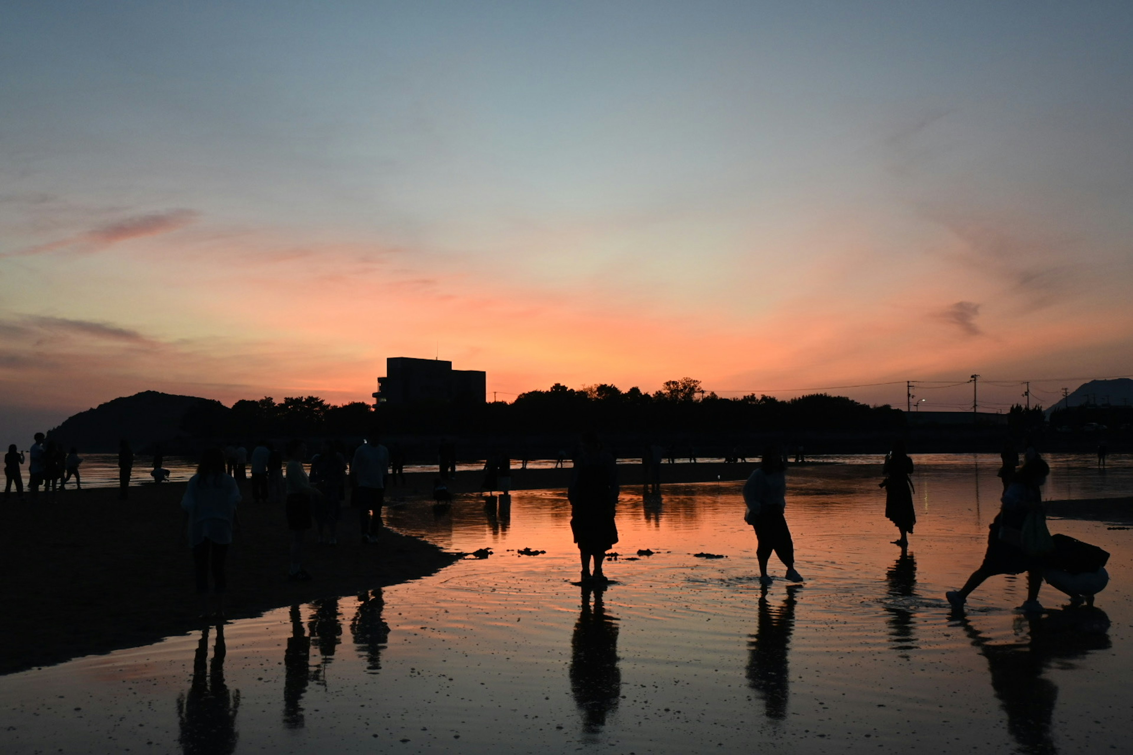 夕焼けの海岸でシルエットの人々が歩いている