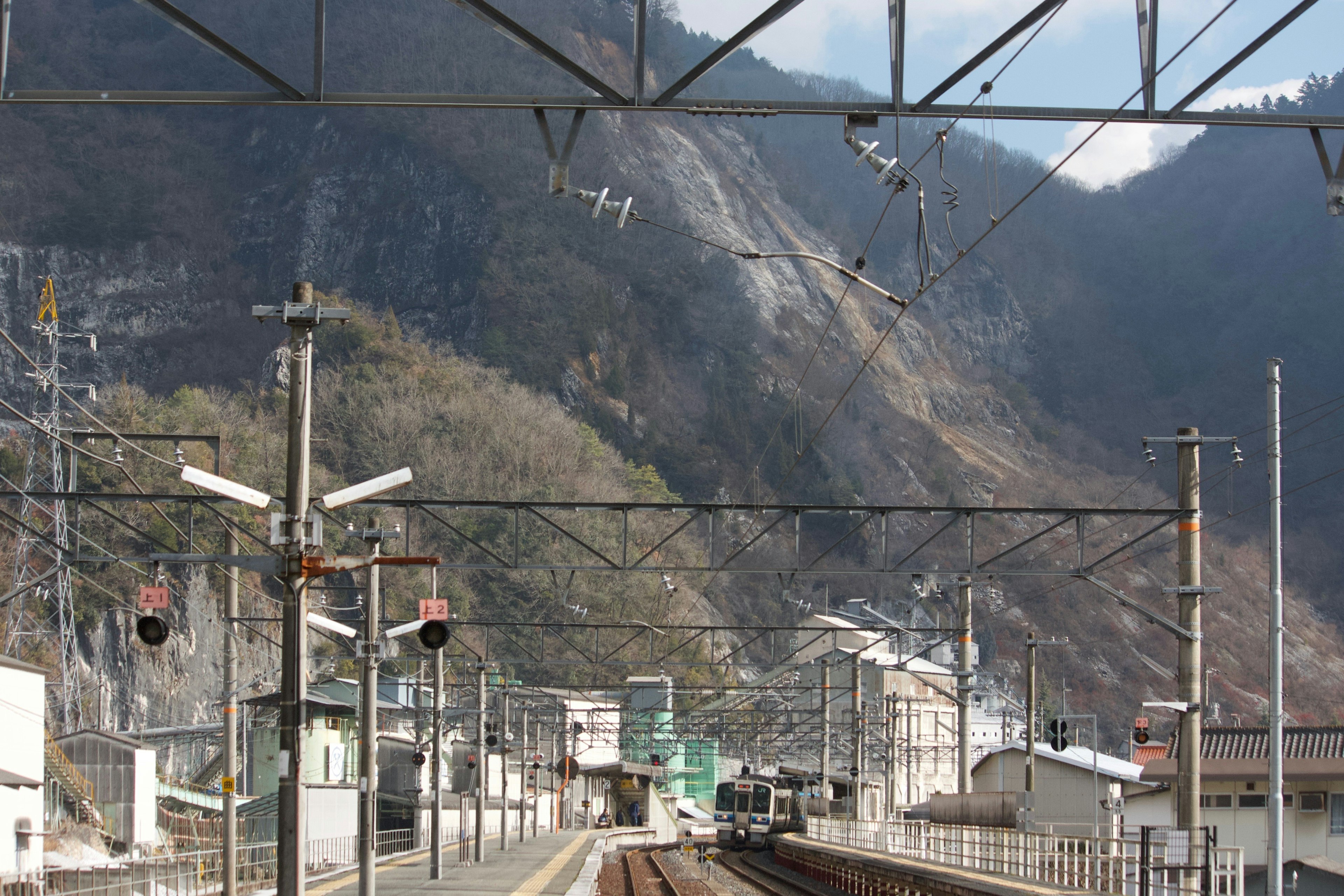 ทิวทัศน์สถานีรถไฟที่ถูกล้อมรอบด้วยภูเขา มีรางรถไฟและสัญญาณ