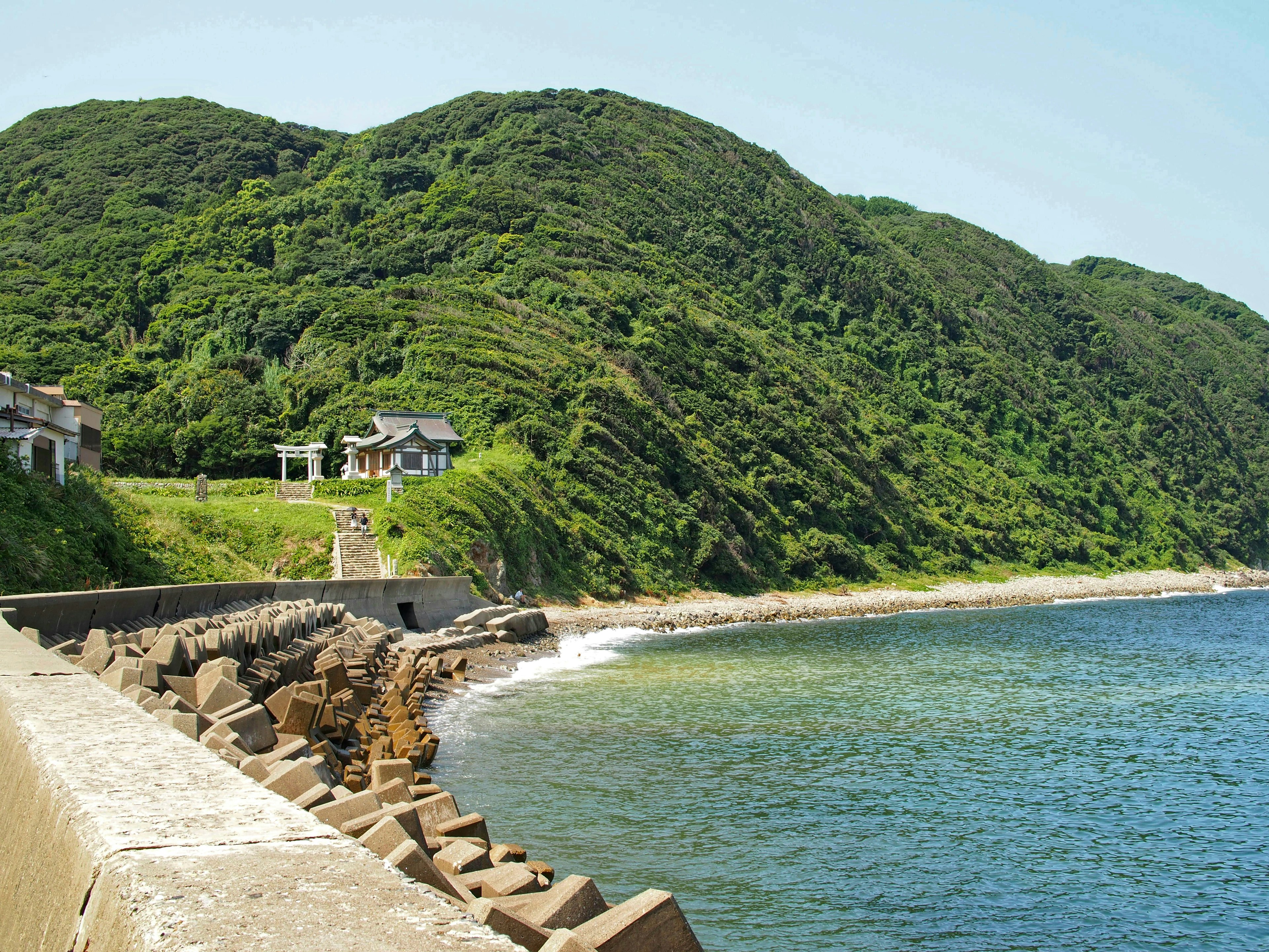 藍色海洋和綠色山丘的風景，海岸邊有石頭堤壩和房子