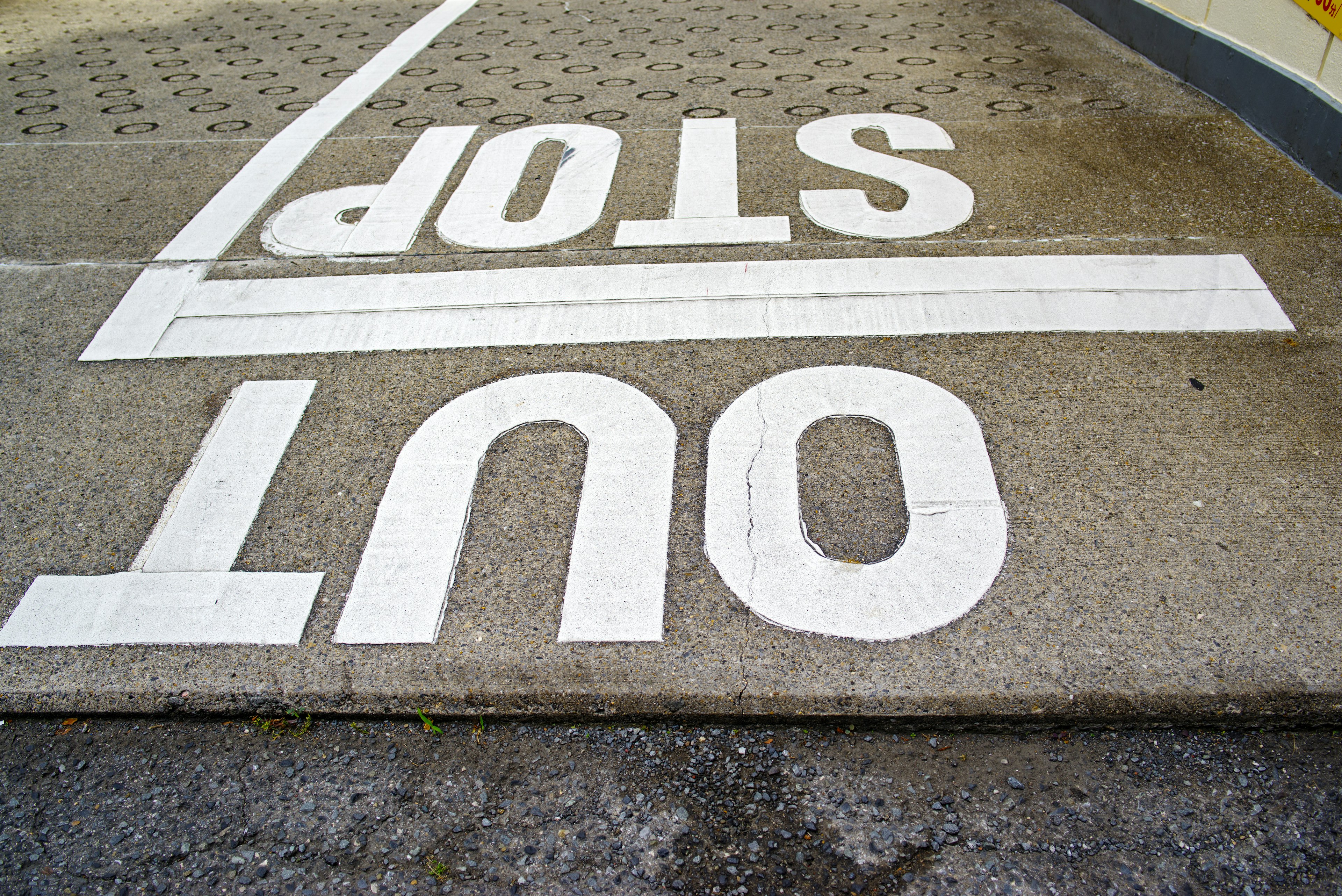 Testo bianco dipinto che legge STOP OUT su una superficie pavimentata