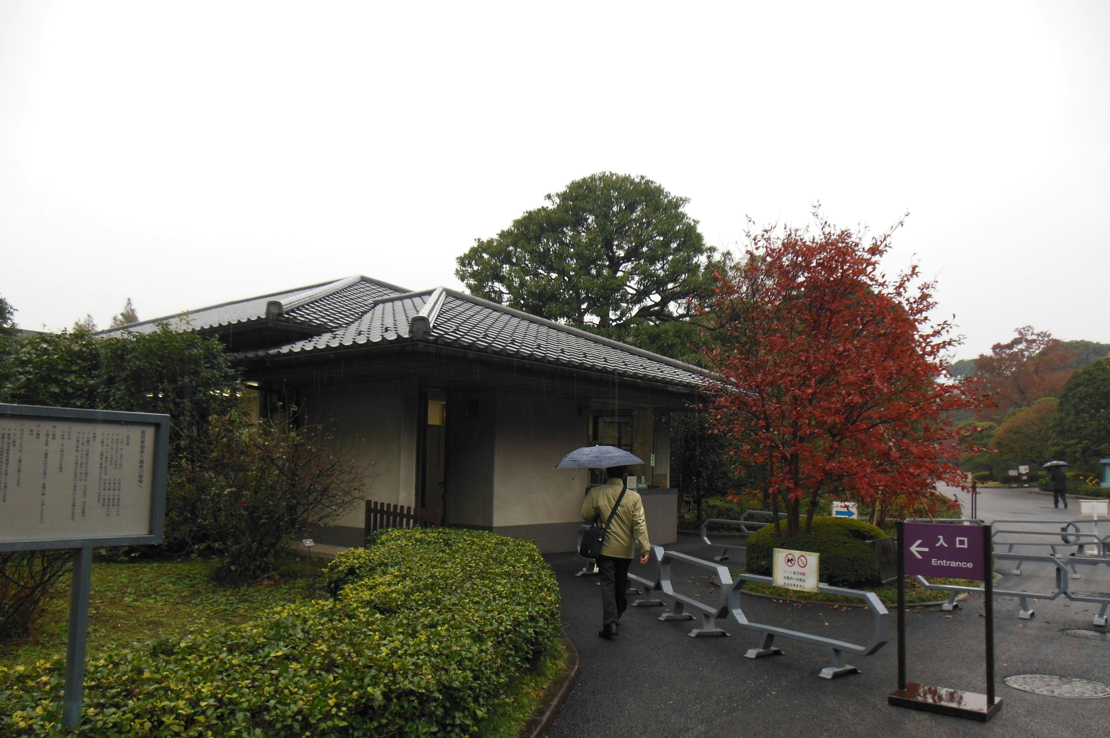 A person holding an umbrella walking towards a traditional Japanese building in the rain