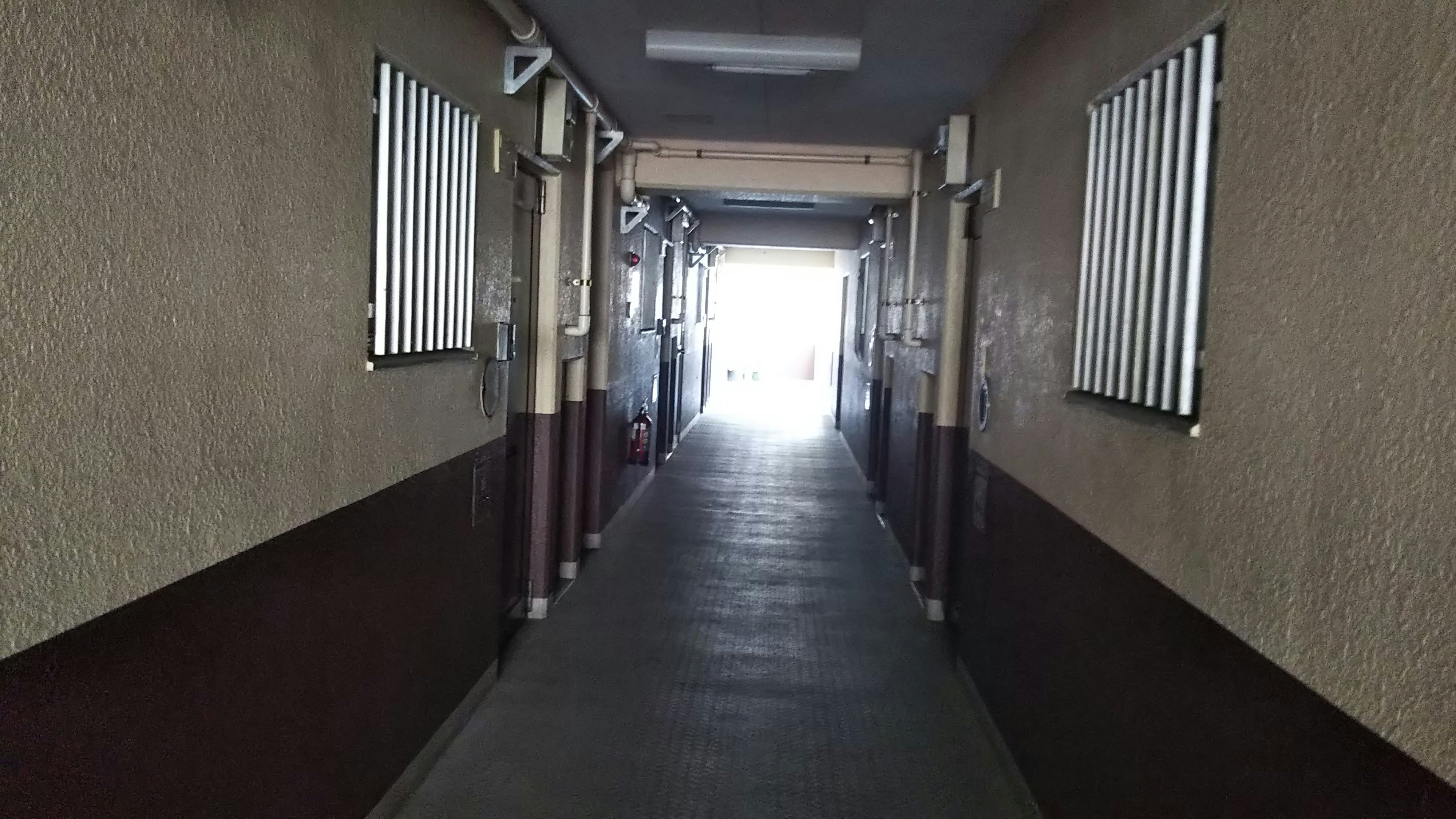 Long corridor leading to bright light with beige walls and concrete floor