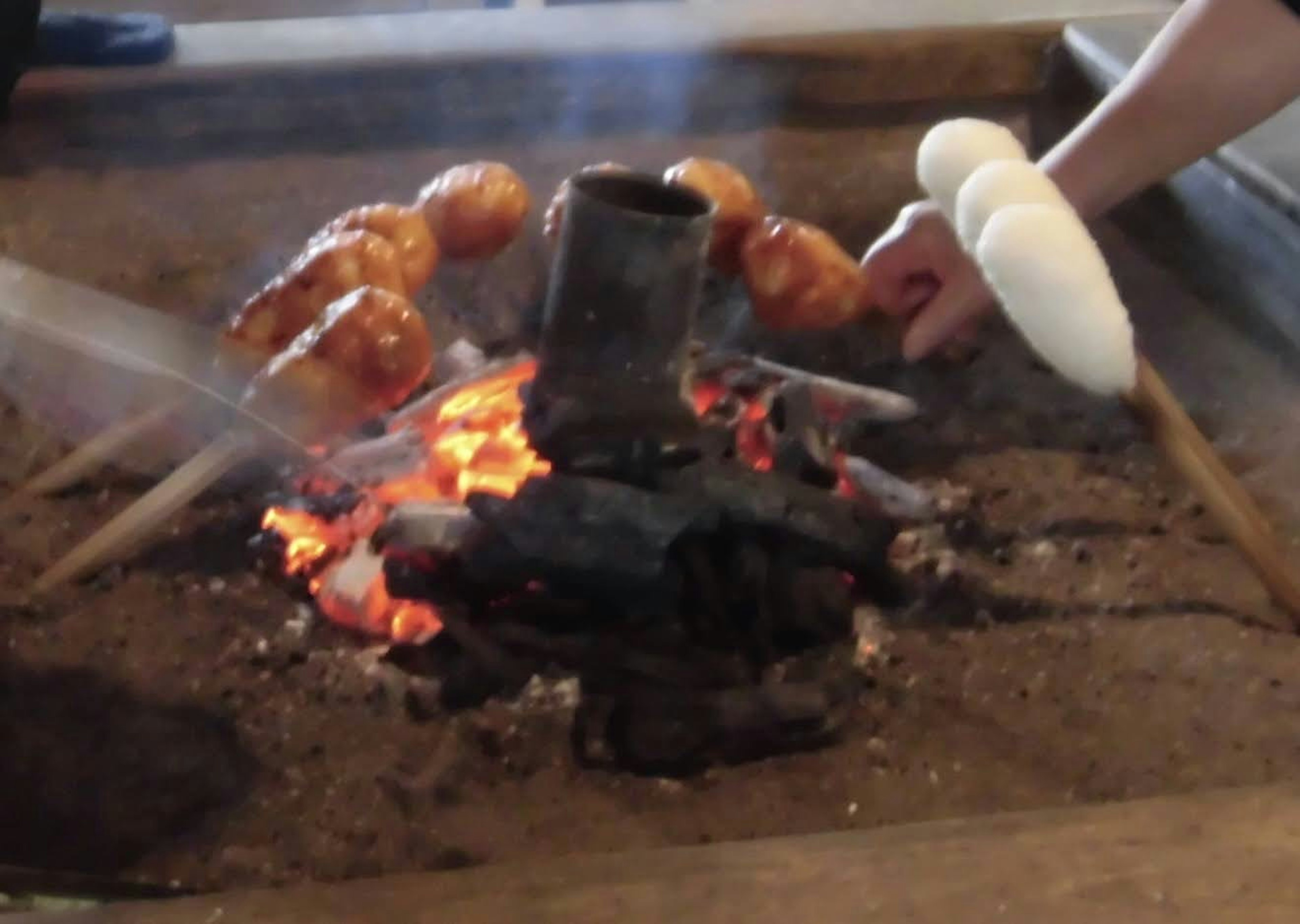 焼き火の中で調理されている食材と手